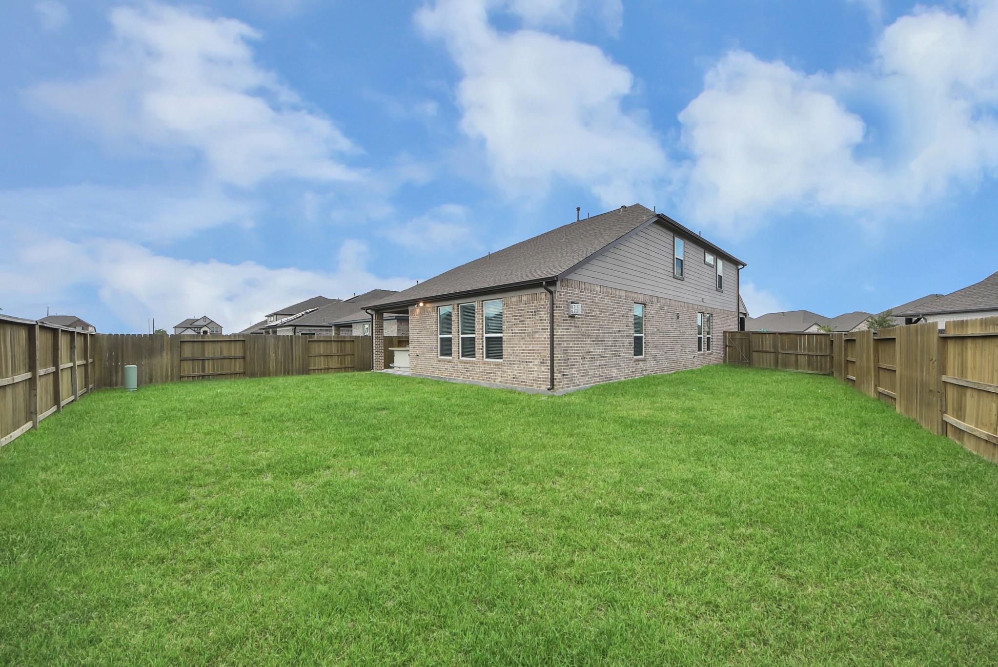 Two-story brick house behind a fenced backyard with a broad green lawn.