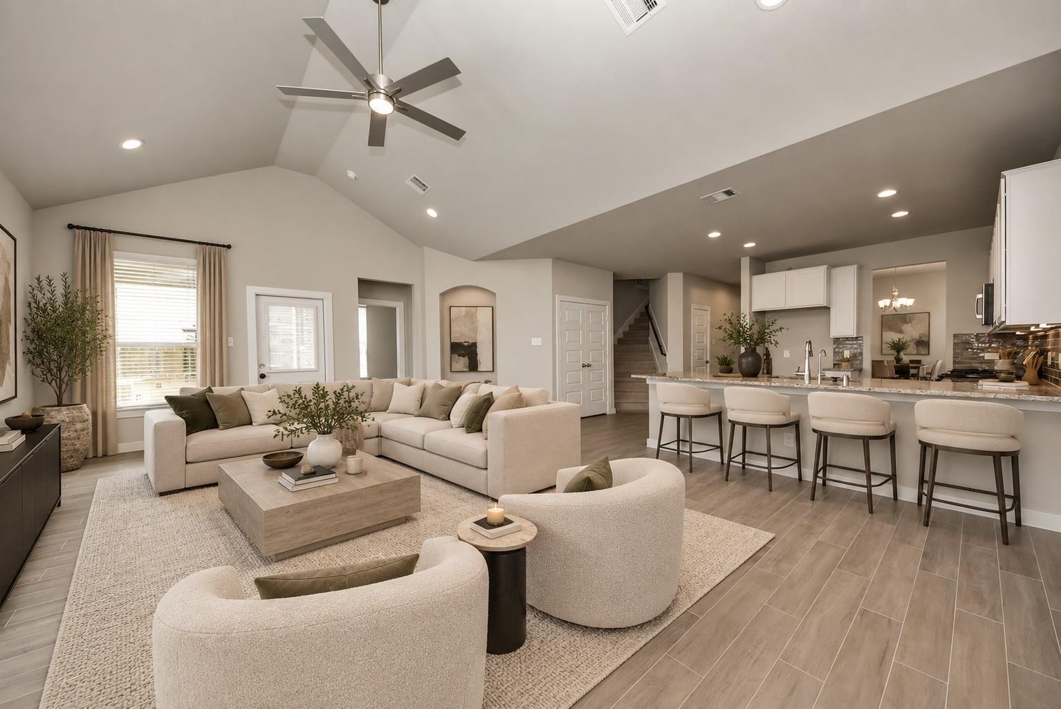 Open-plan living room and kitchen with a vaulted ceiling, sectional sofa, island seating, and staircase.