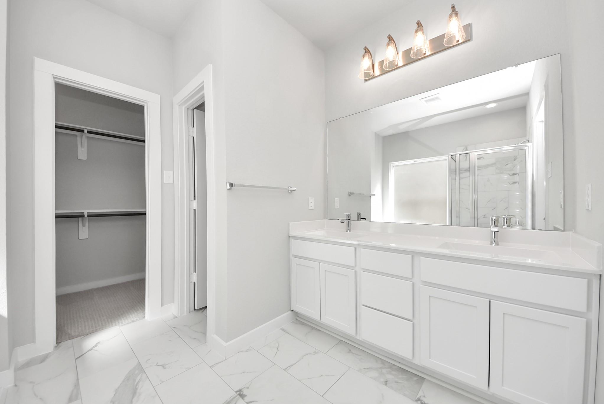 Bathroom with a white double vanity, marble-look tile floor, and walk-in closet doorway.
