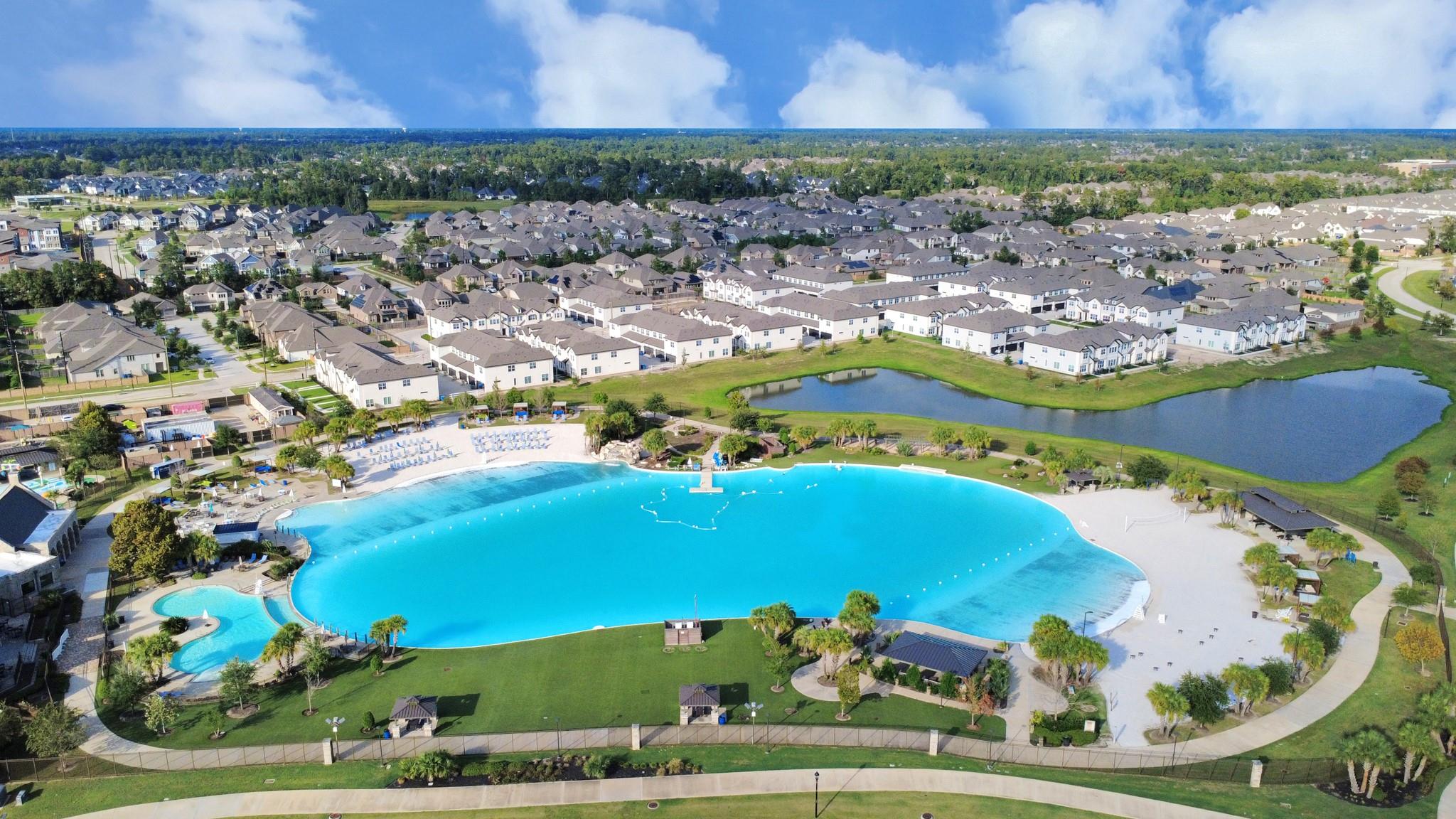 Aerial view of a neighborhood lagoon-style pool, surrounding homes, and pond.