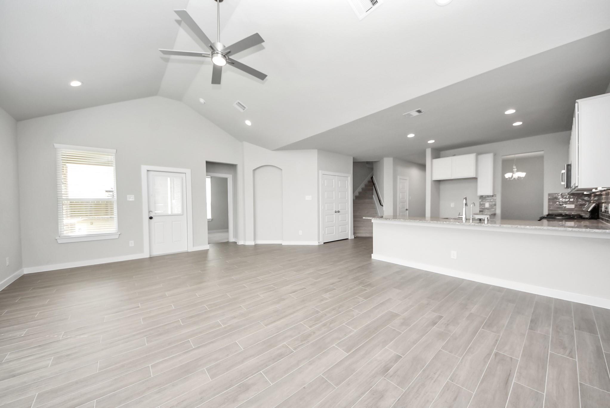 Empty open-plan living room and kitchen with gray tile floors, vaulted ceiling, and long breakfast bar.