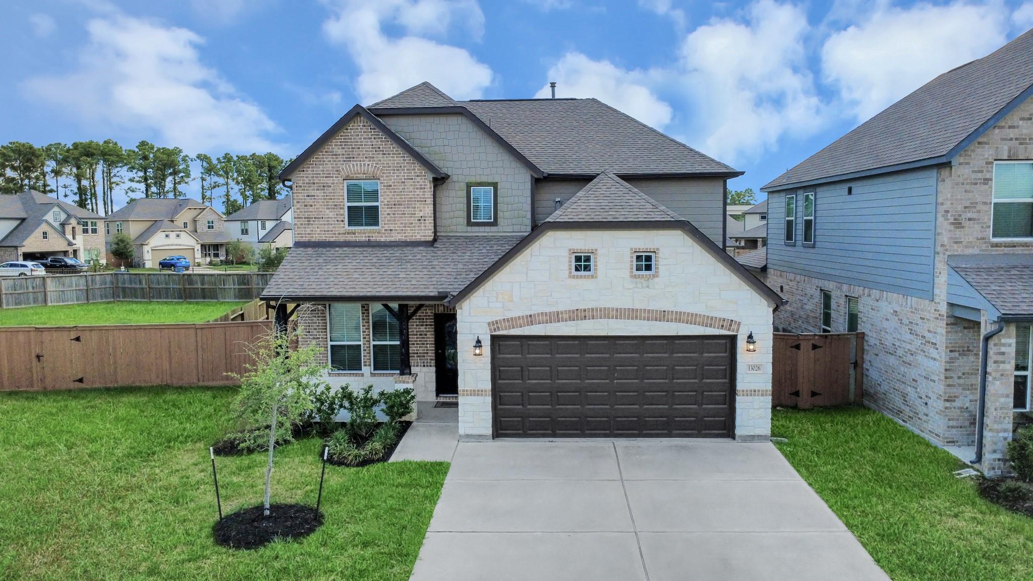 Two-story brick and stone home with a dark double garage, wide driveway, and fenced lawn.