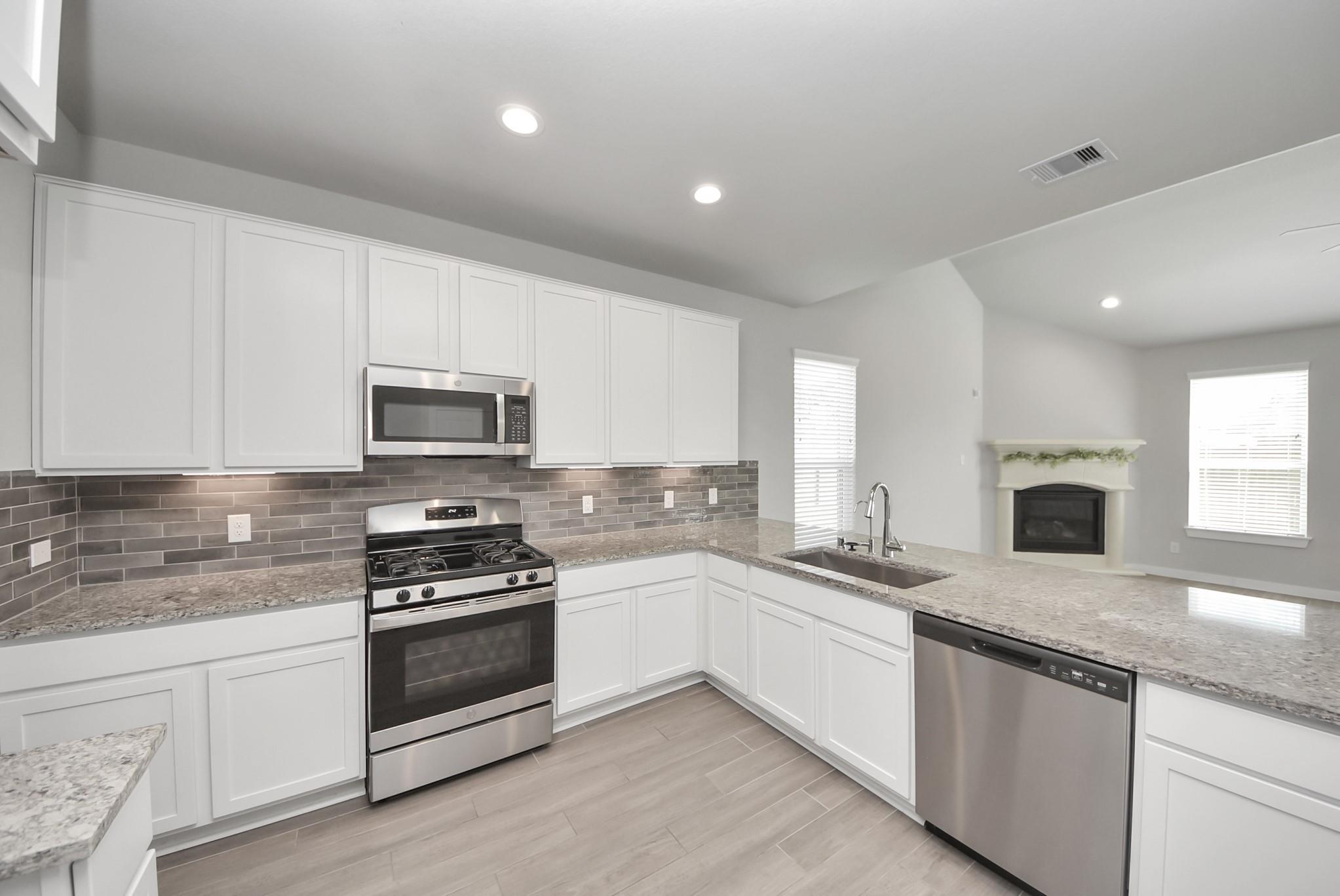 Kitchen with white cabinets, granite counters, stainless appliances, and an open view of a fireplace.