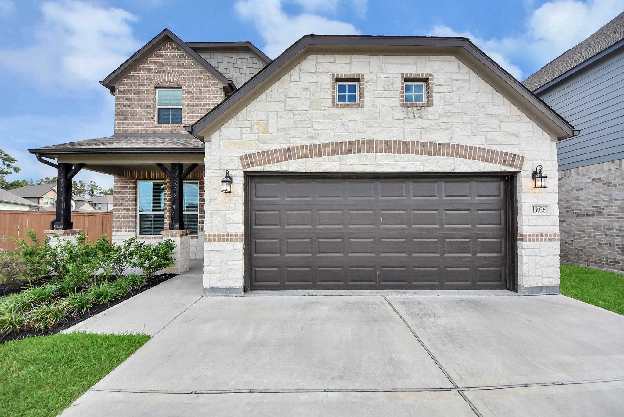 Two-story stone-and-brick house with a covered porch, dark double garage door, and broad driveway.