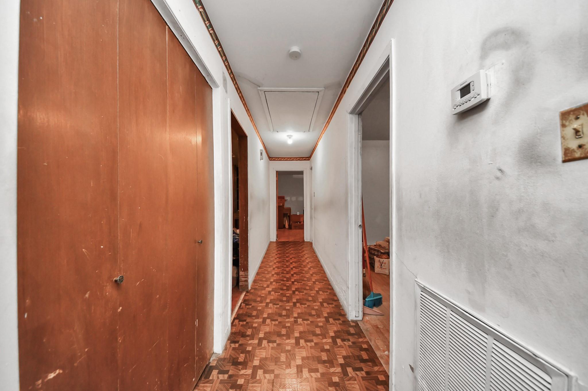 Narrow hallway with parquet flooring, large wood-paneled closet doors, and open doorways.