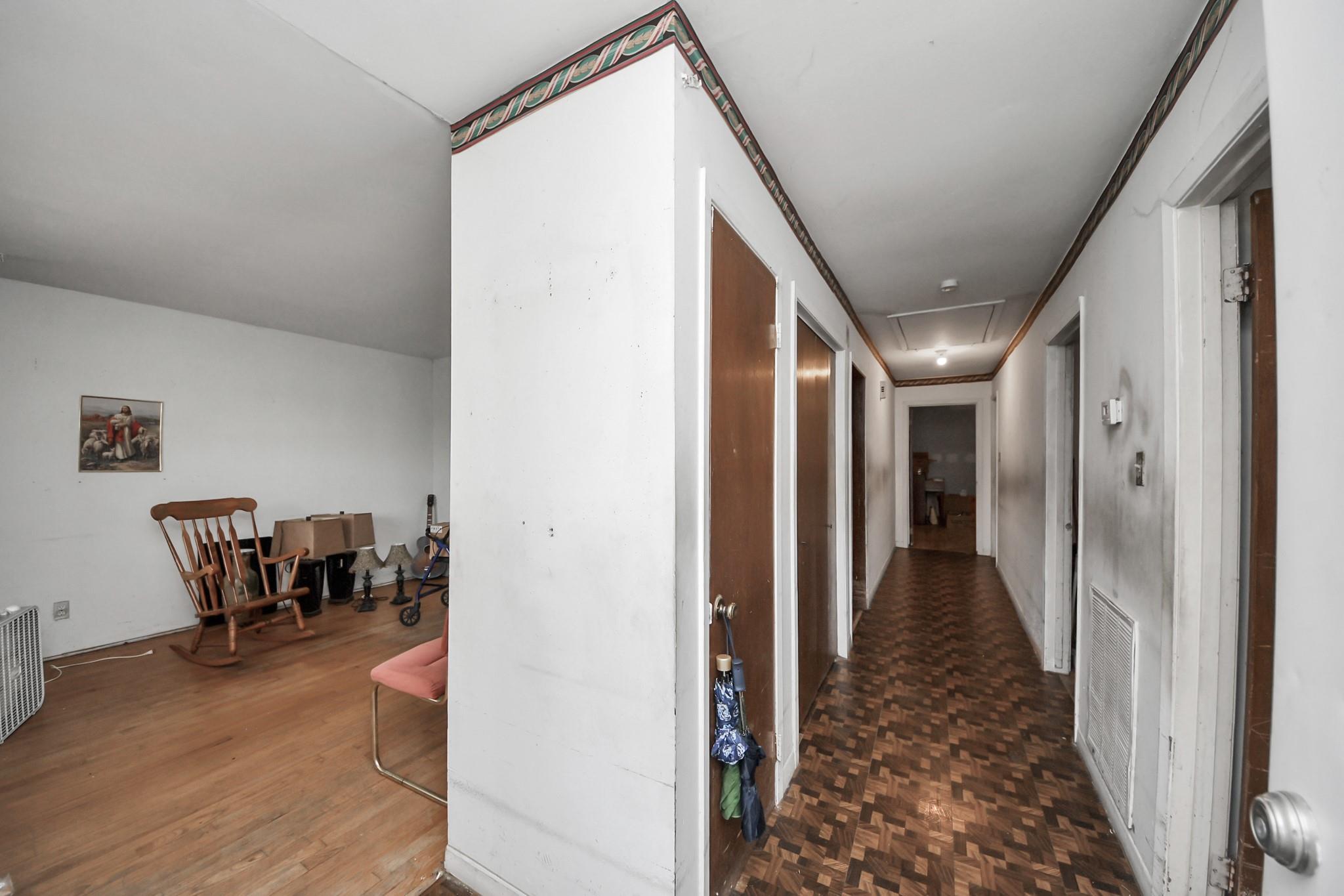 Hallway with patterned parquet flooring beside a sitting room with a wooden rocking chair.