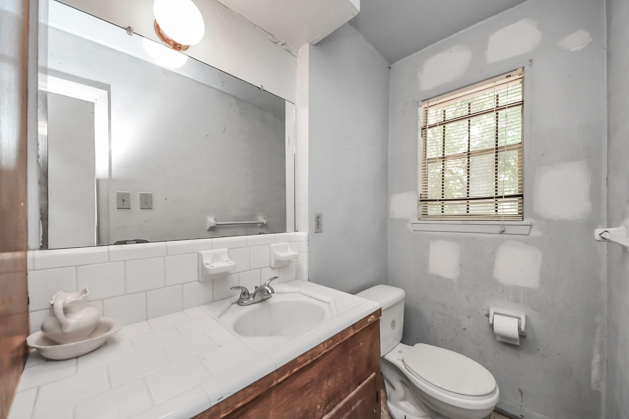 Bathroom with tiled vanity, large mirror, toilet, and a window with blinds.