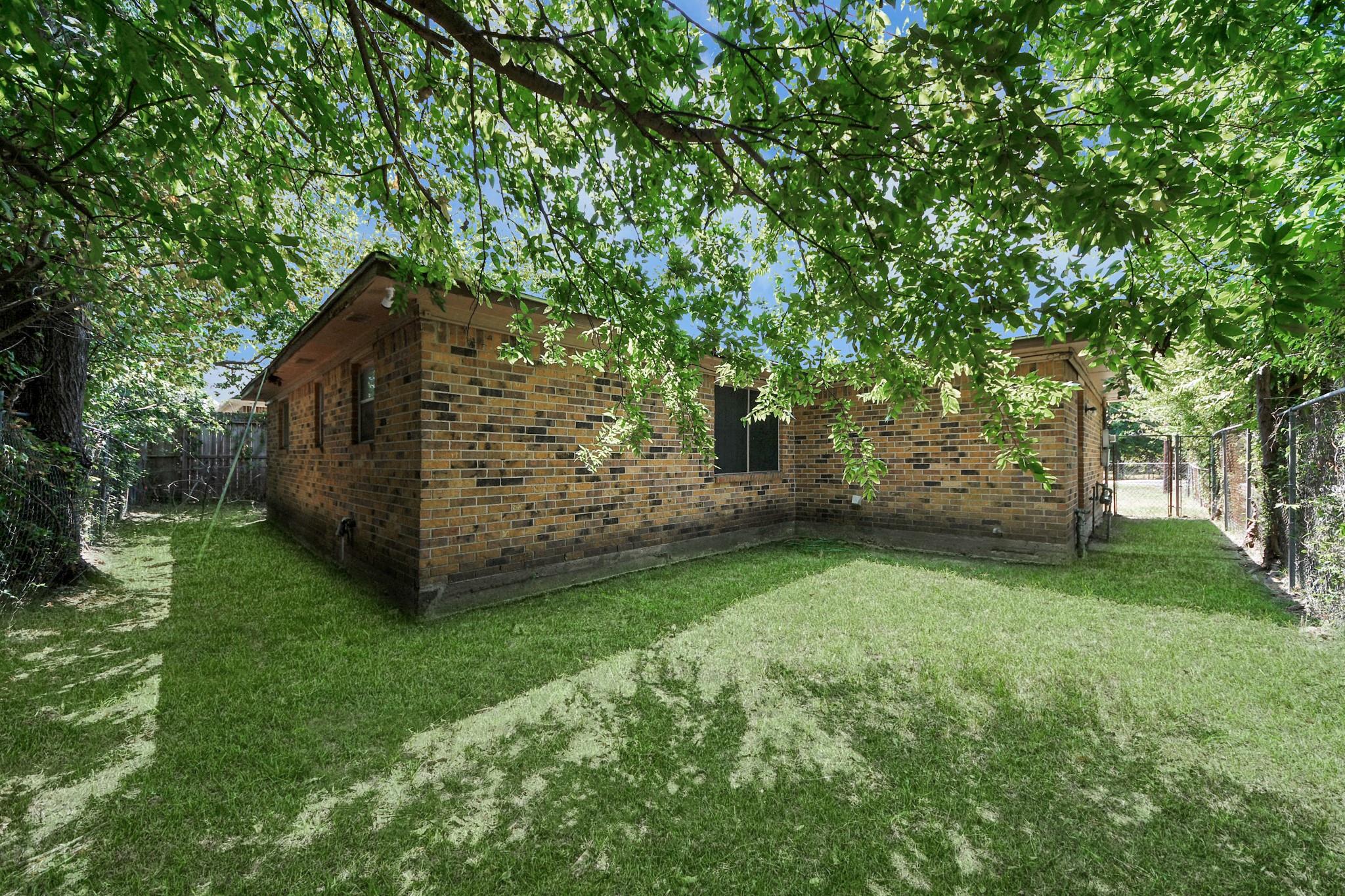 Brick house at the back of a grassy yard shaded by mature trees.