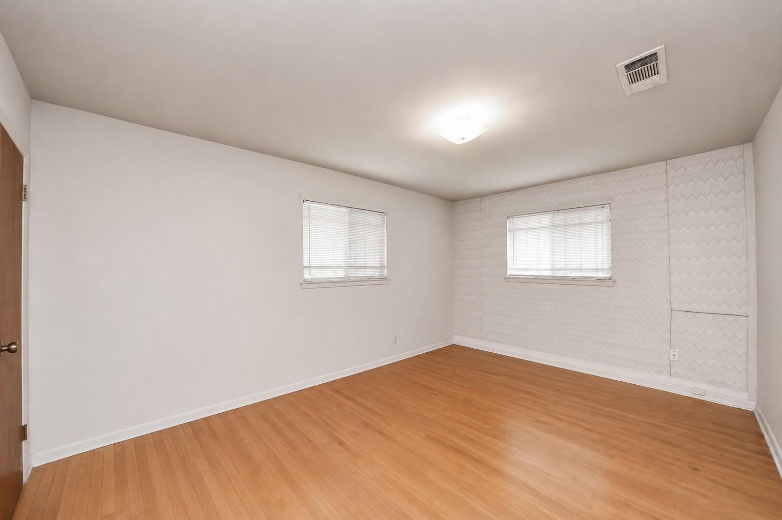 Empty room with hardwood floors, two windows, and a pale chevron-patterned wall.
