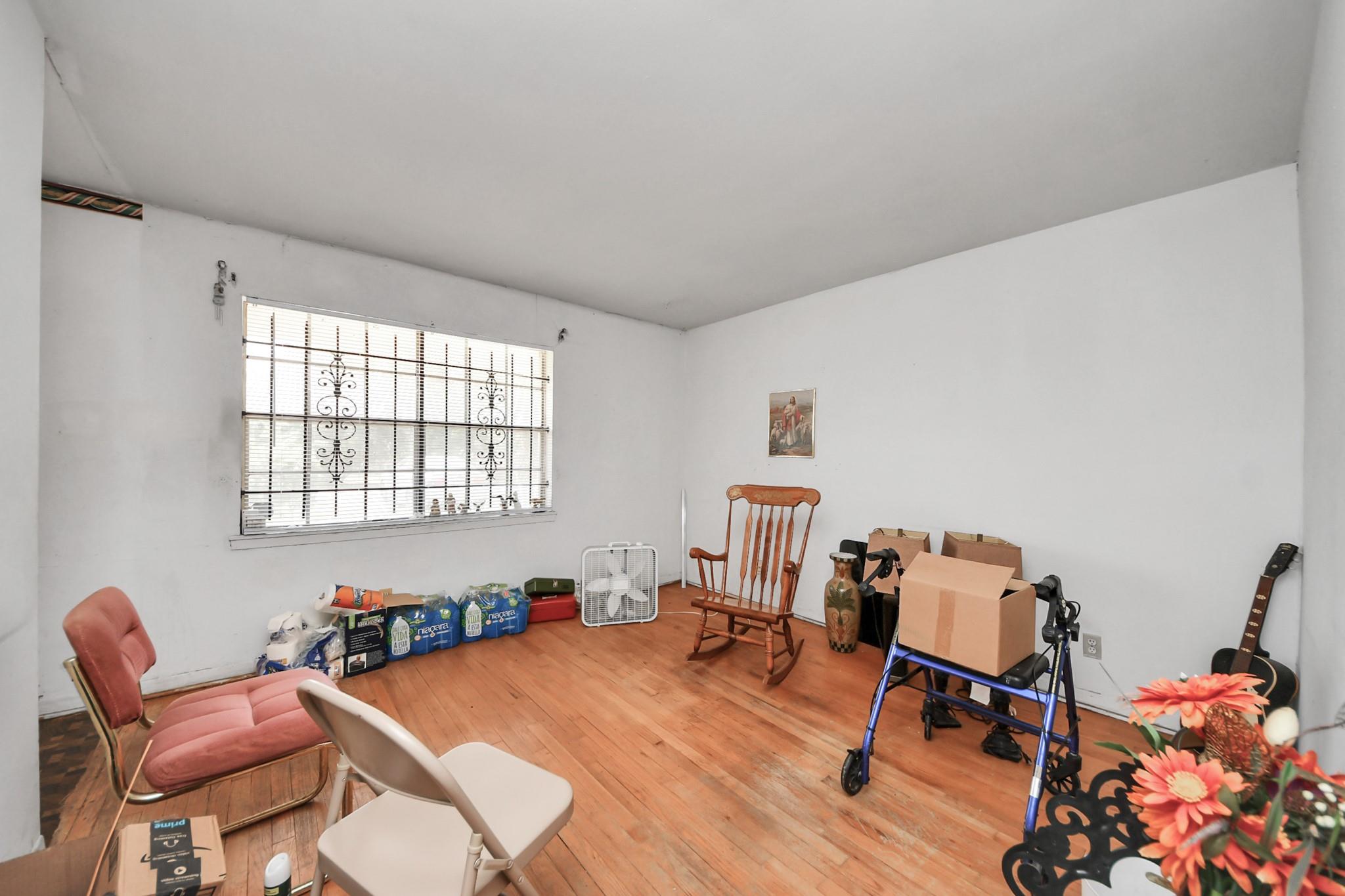 Room with hardwood floors, a barred window, assorted chairs, boxes, and household items.