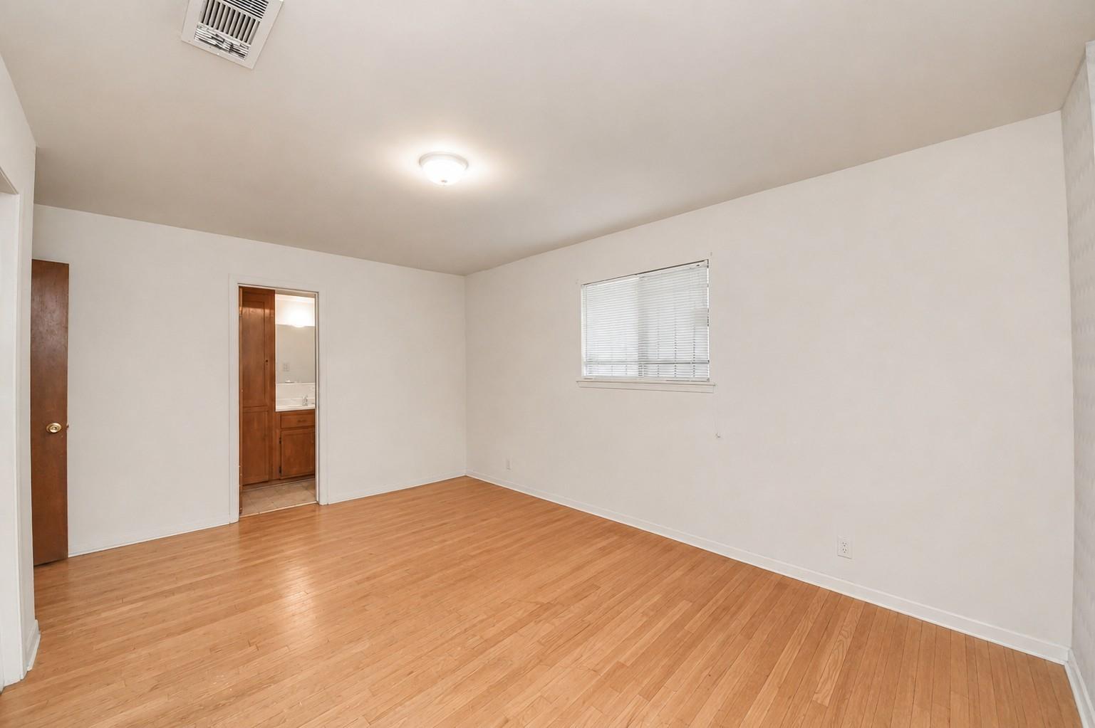 Empty bedroom with light wood floors and a doorway to a bathroom with wood cabinetry.