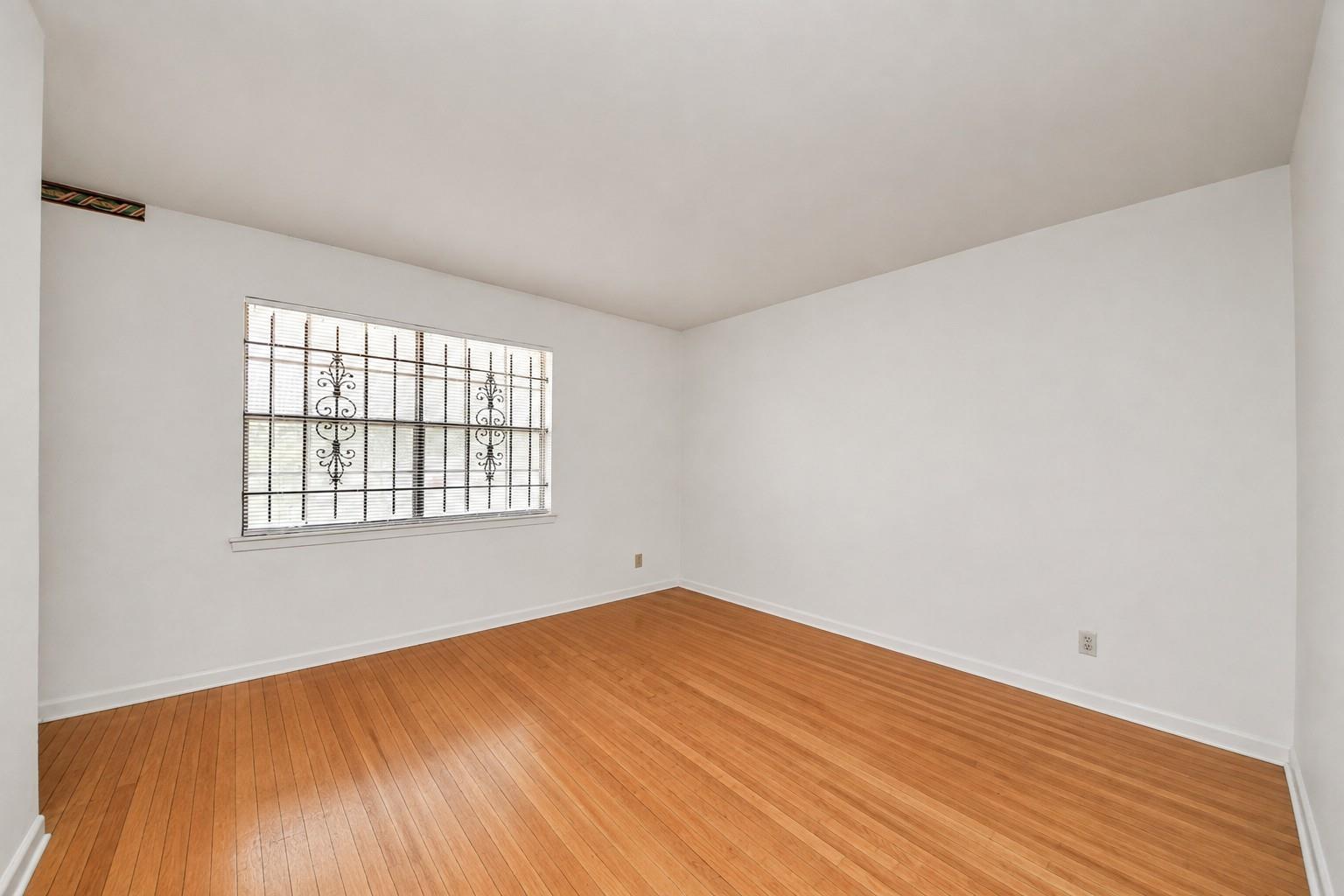 Empty room with hardwood floors and a window with decorative metal bars.