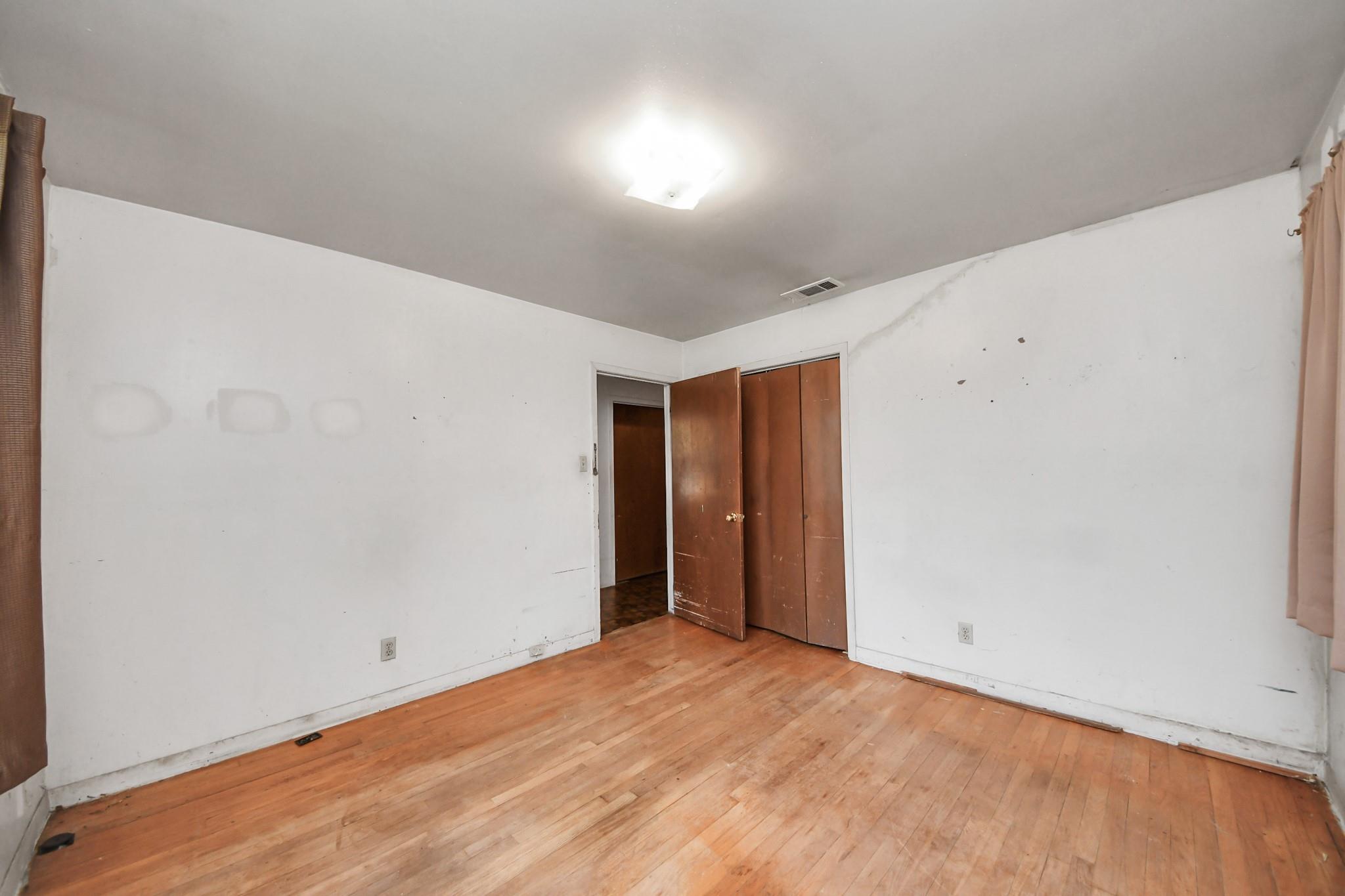 Empty bedroom with hardwood floors, marked white walls, and brown closet doors.
