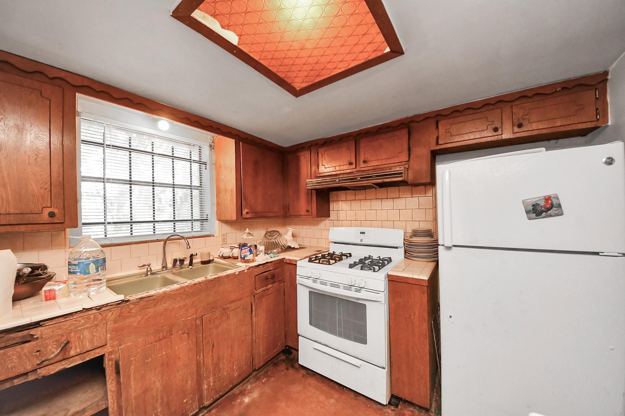 Kitchen with reddish-brown wood cabinets, a window over the sink, and white gas range and refrigerator.