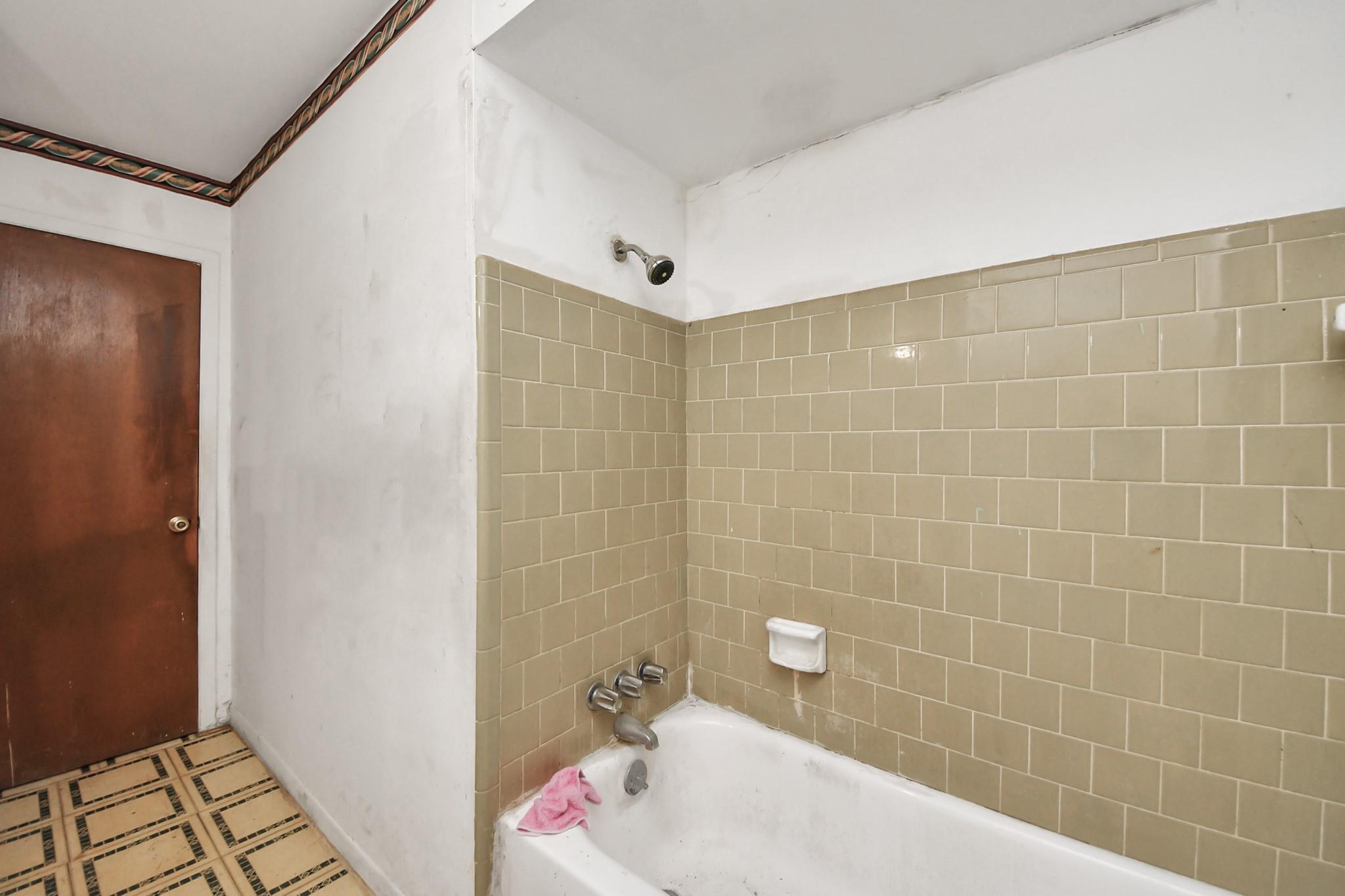Bathroom with beige tiled tub and shower, chrome fixtures, and a patterned tile floor.