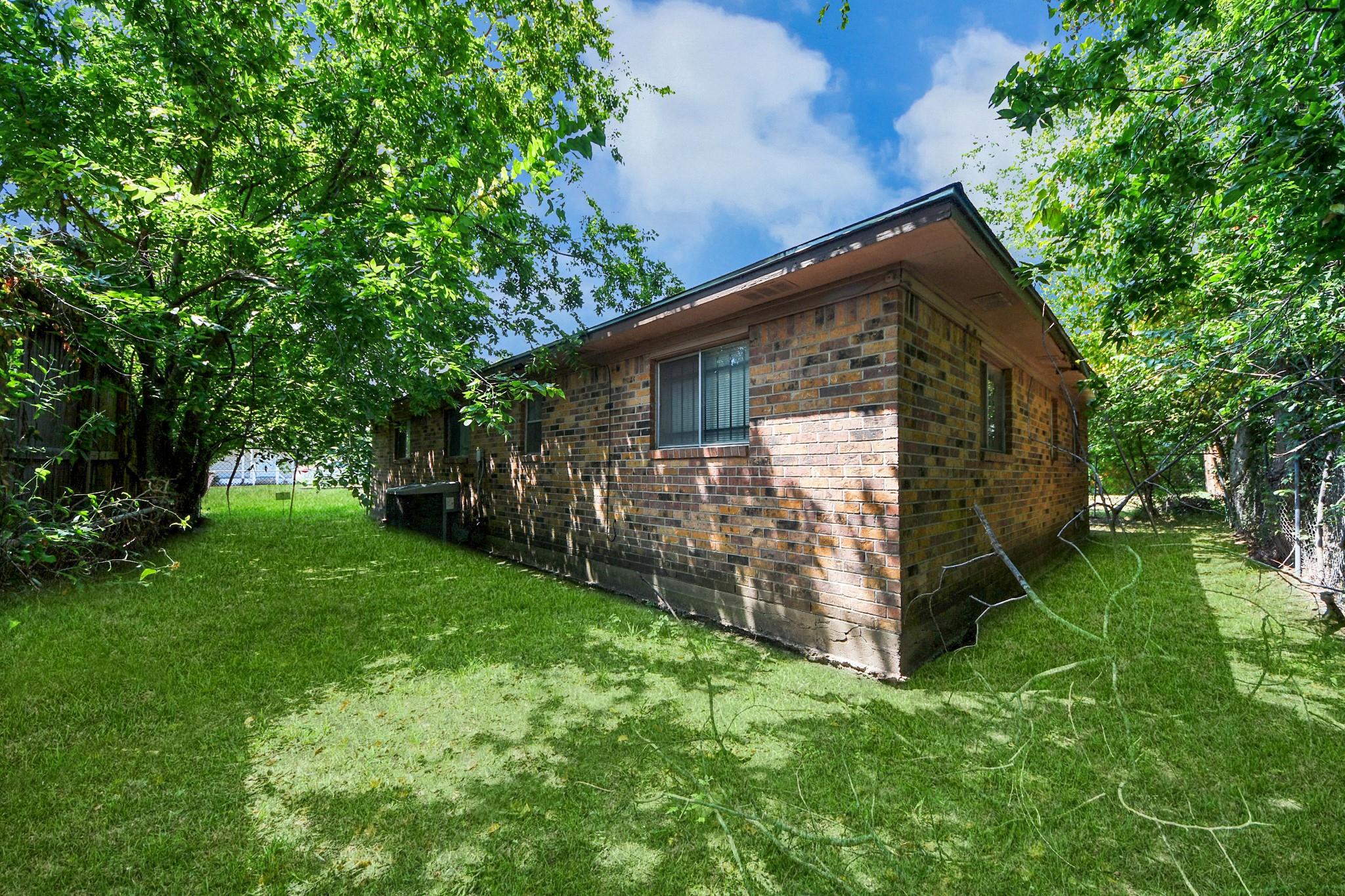 Brick house side exterior beside a shaded lawn and mature trees.