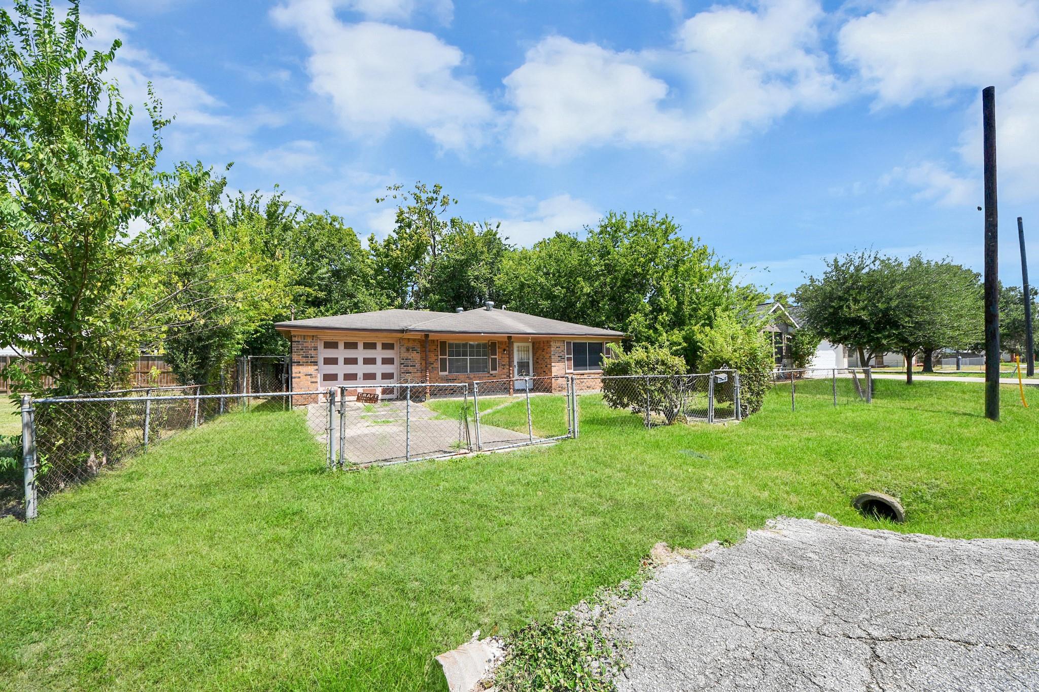 Single-story brick home behind a chain-link fence, with a front lawn and attached garage.