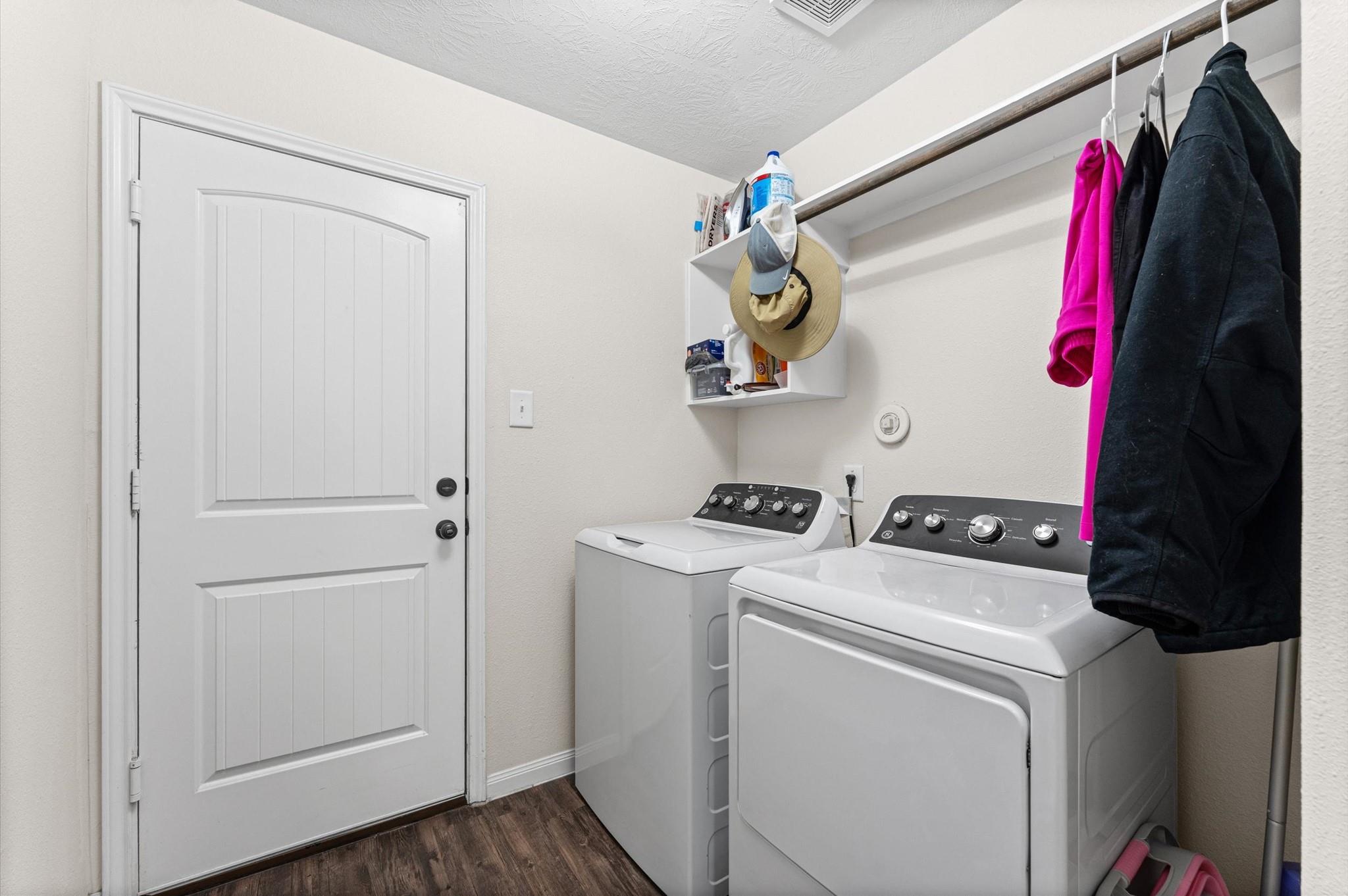 Laundry room with a white washer and dryer, hanging clothes, and wall-mounted shelves.