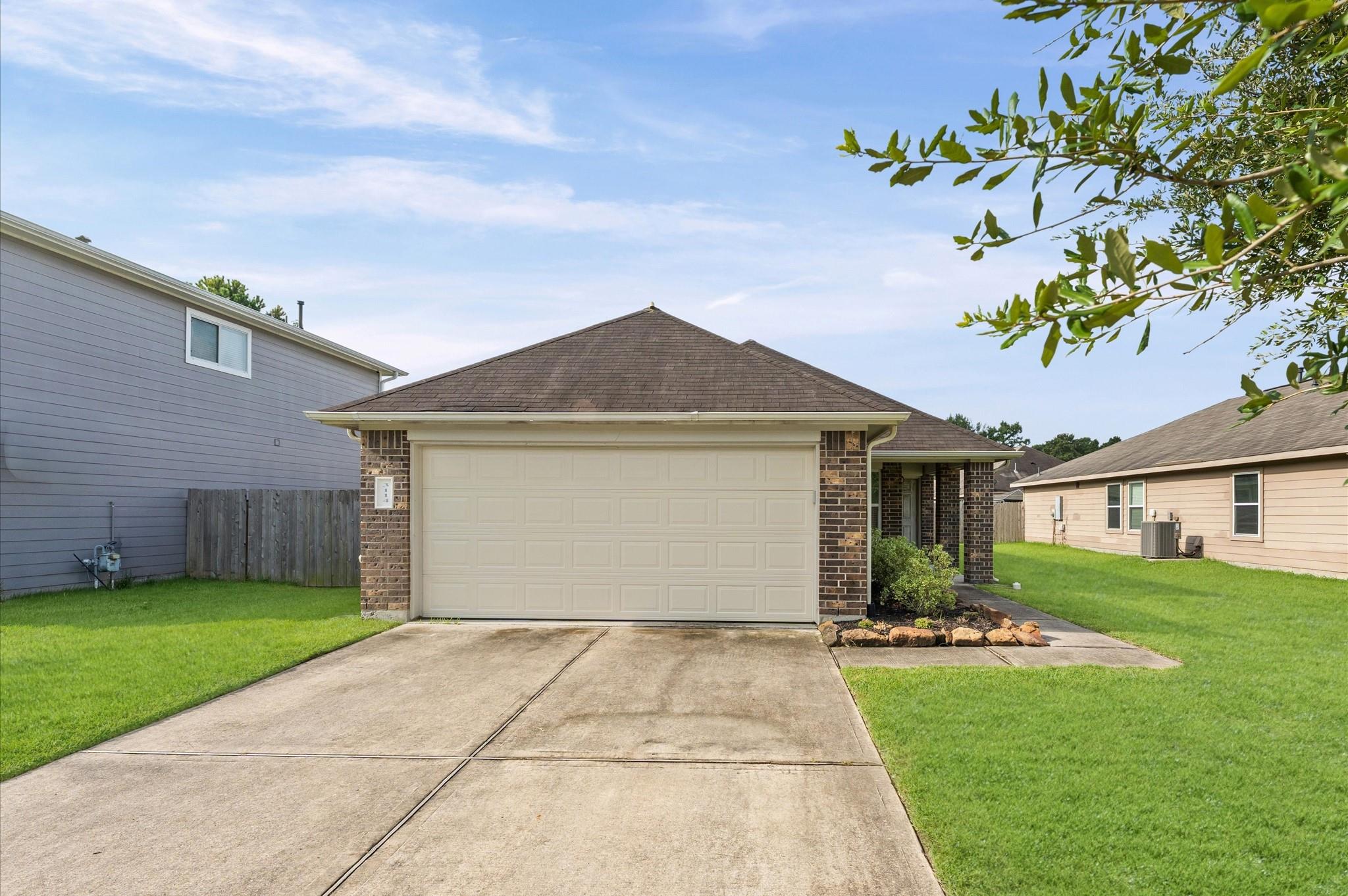 House with a wide two-car garage, brick accents, concrete driveway, and green lawn.
