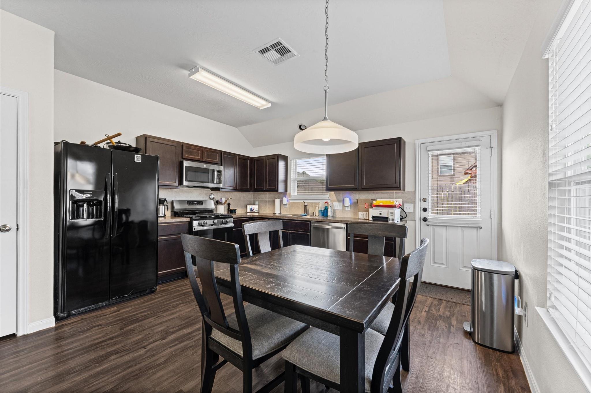 Kitchen with dark wood cabinets, black appliances, and a dining table beside a glass door.