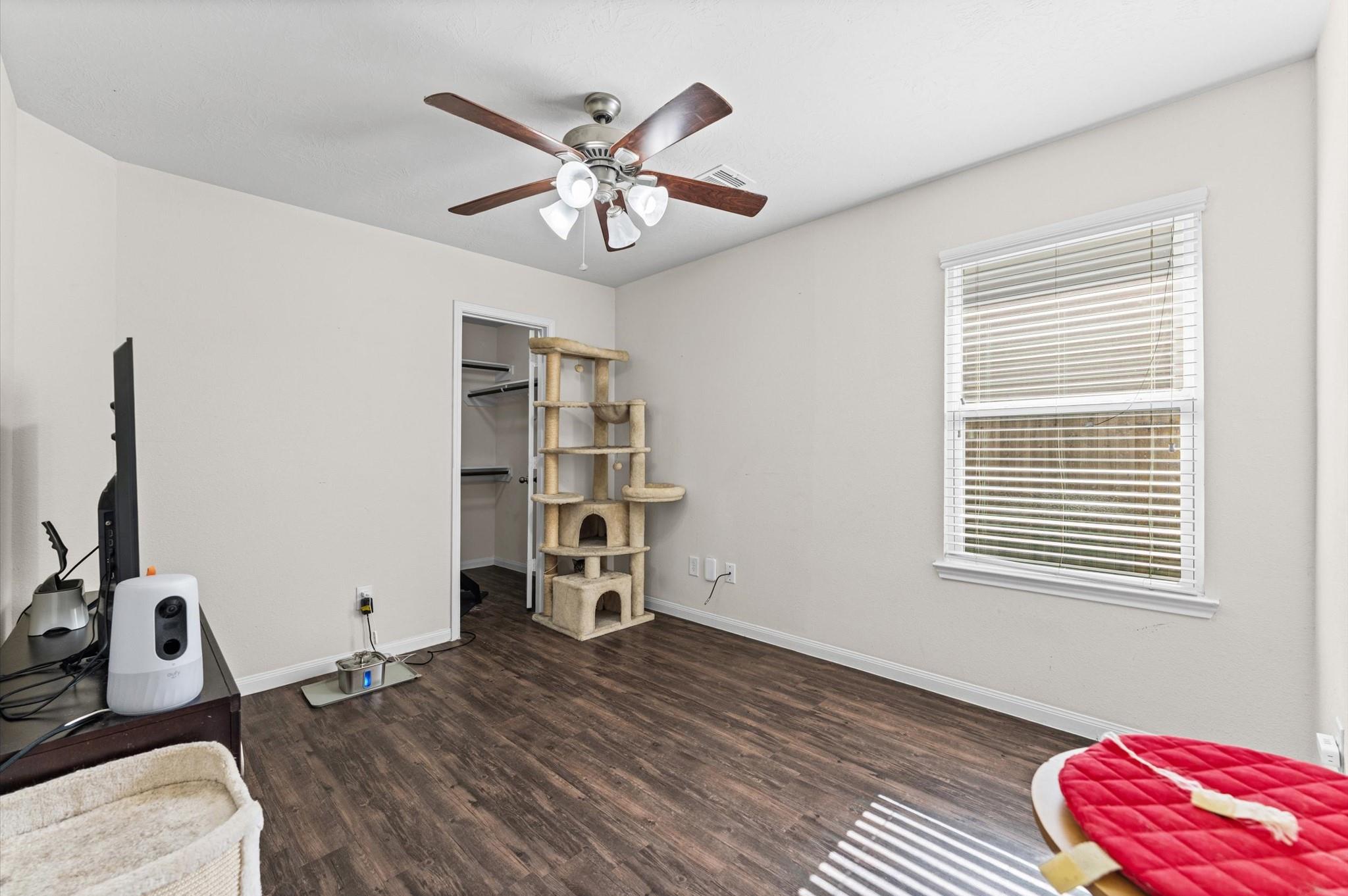 Bedroom with dark flooring, a large cat tree beside the closet, and a window with white blinds.