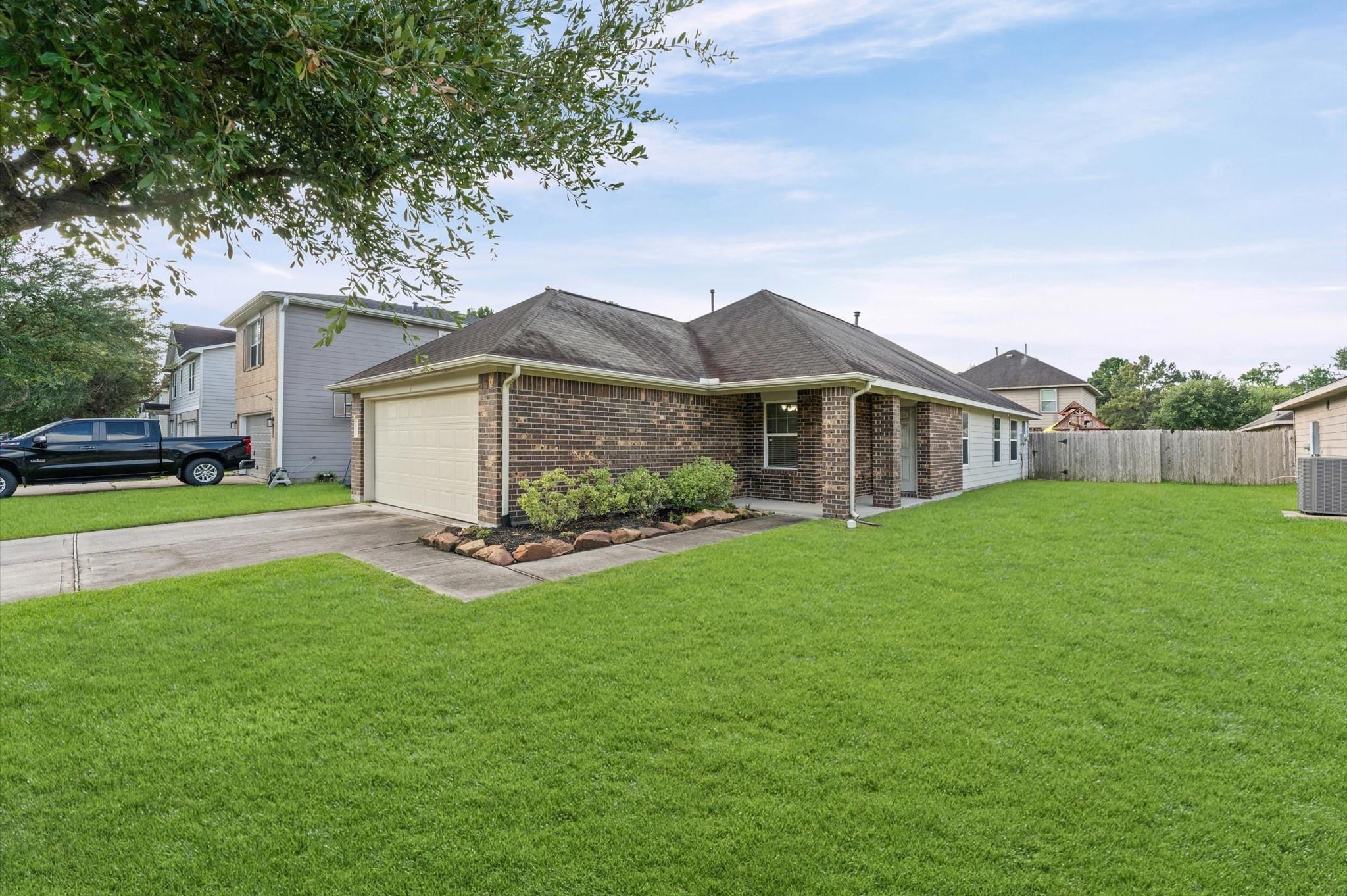 Single-story brick house with a two-car garage, landscaped front bed, and broad green lawn.