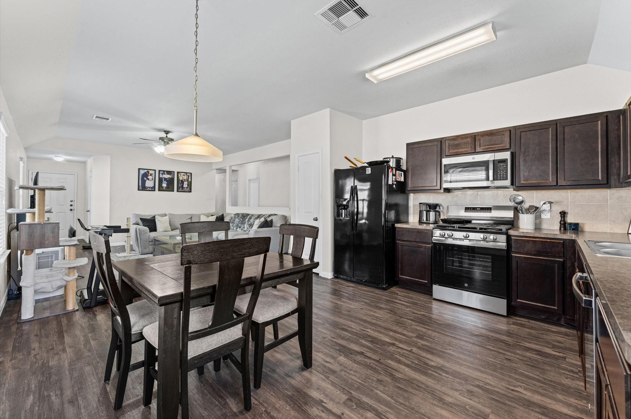 Open kitchen and dining area with dark cabinetry, stainless appliances, and adjoining living room.