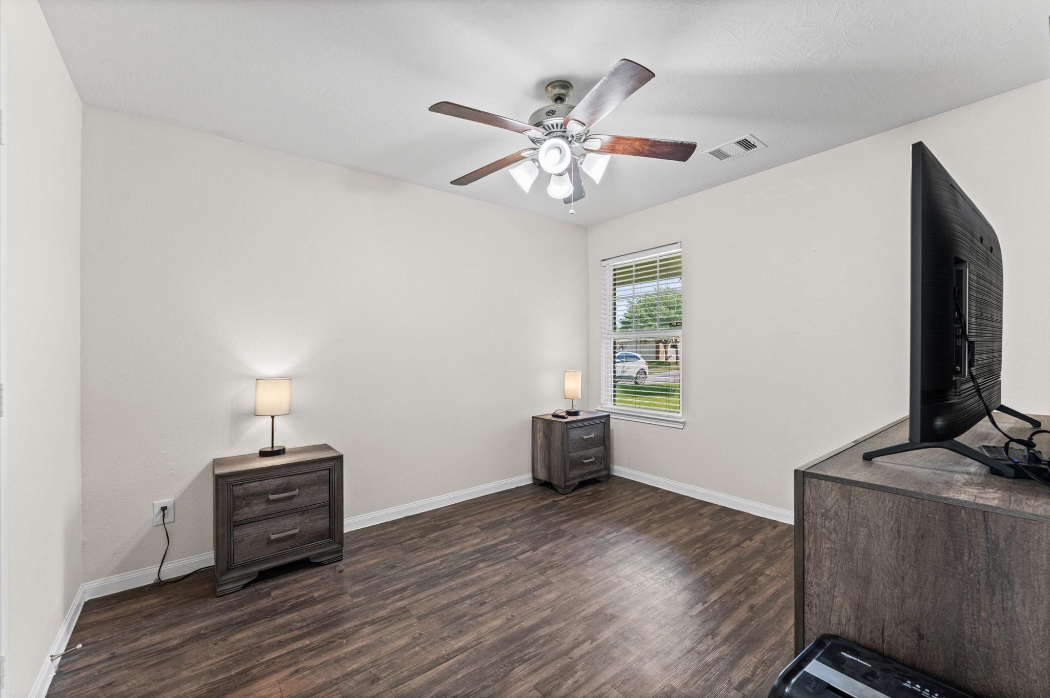 Furnished room with dark wood-look floors, a ceiling fan, and a window with blinds.