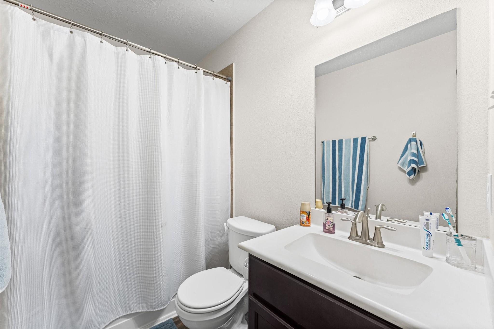 Bathroom with a white shower curtain, toilet, and dark vanity with a large mirror and striped blue towels.