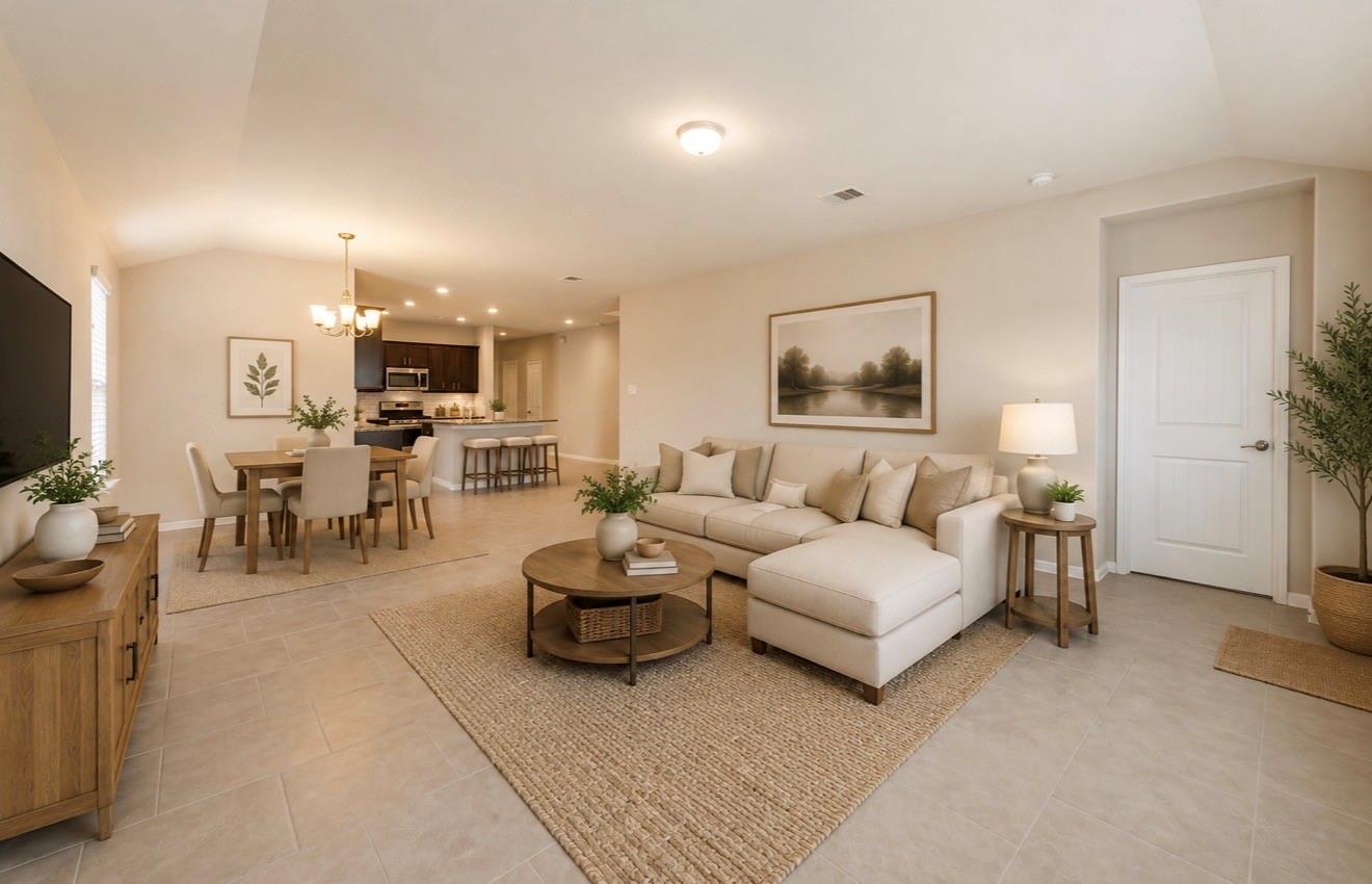 Open-plan living and dining room with a cream sectional, woven rug, dining table, and kitchen beyond.