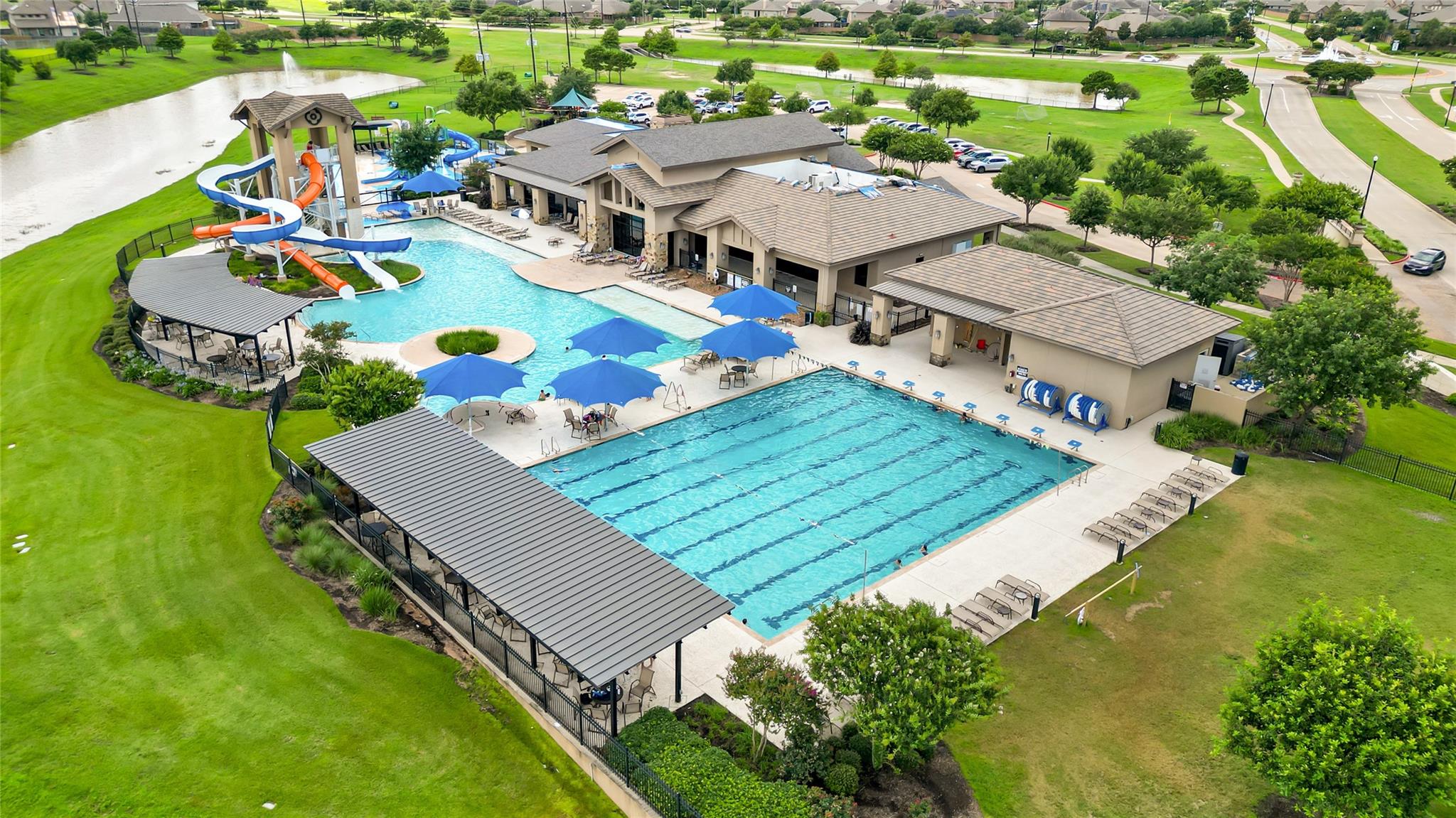 Community pool complex with lap lanes, water slides, shaded seating, and expansive green lawns.