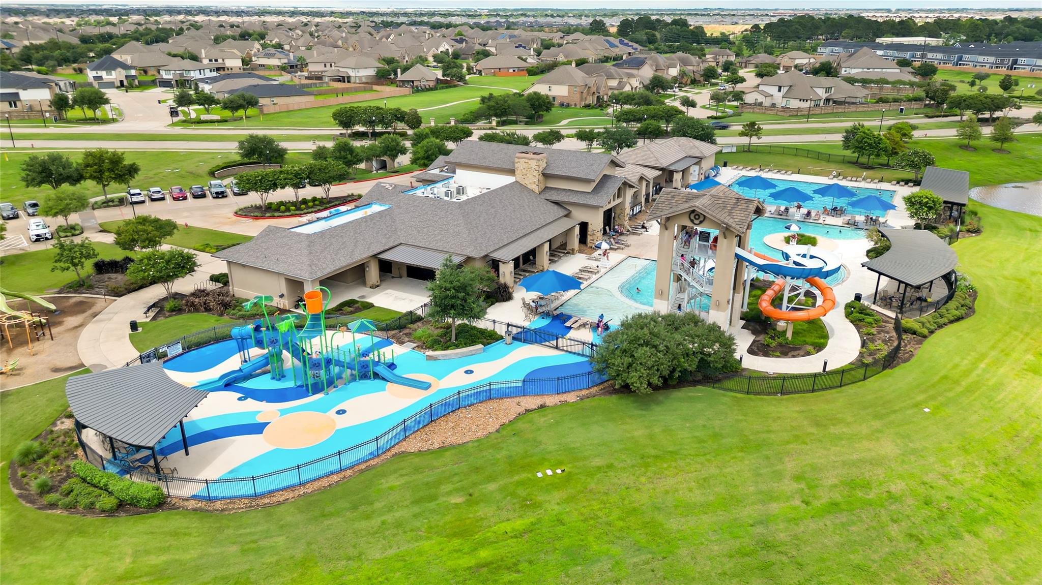 Community pool complex with water slides, a colorful splash pad, and surrounding neighborhood homes.