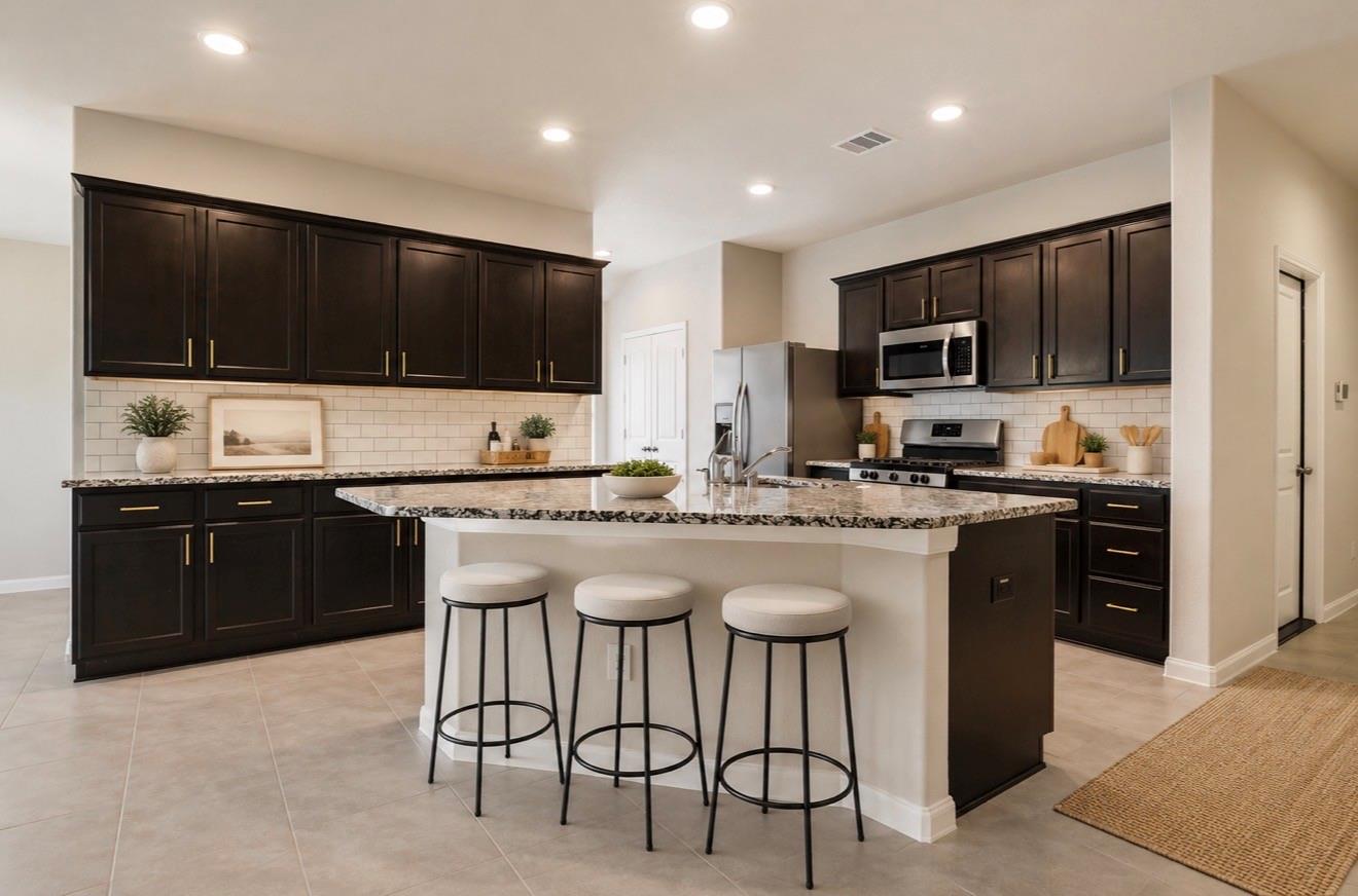 Kitchen with dark cabinets, stainless steel appliances, and a granite island with three stools.