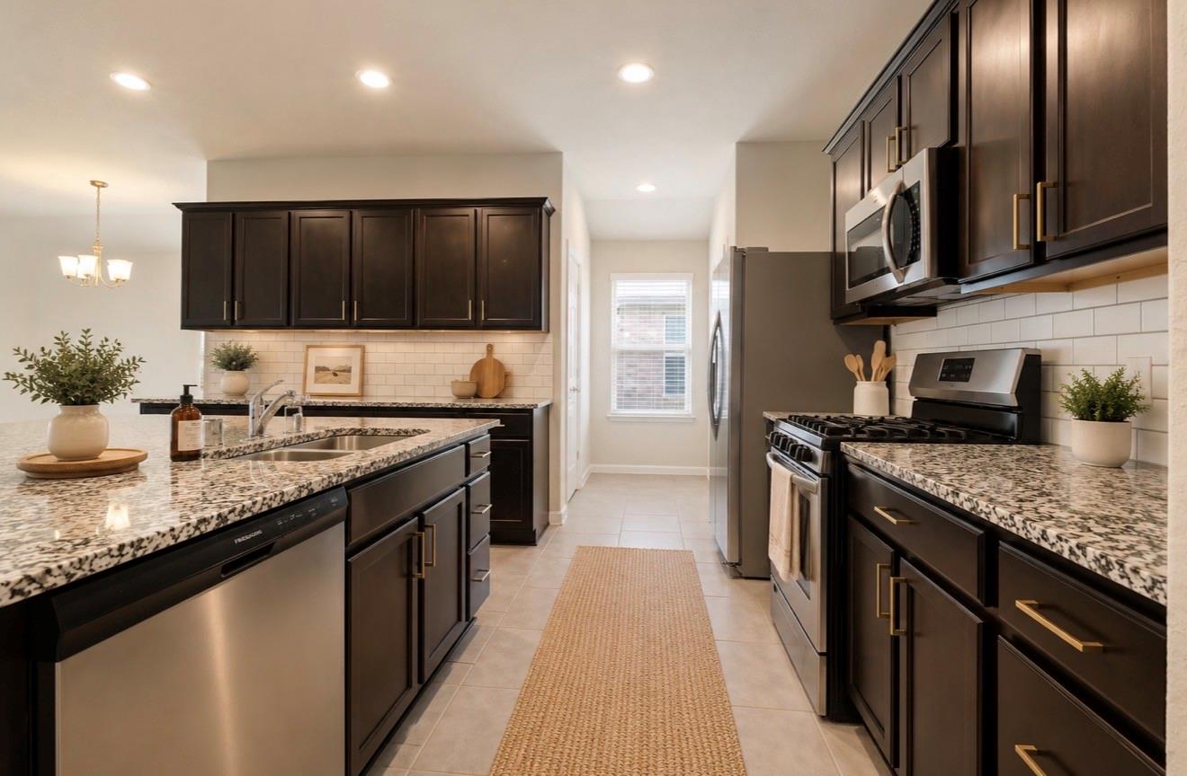 Galley kitchen with dark cabinets, granite counters, and stainless steel appliances.
