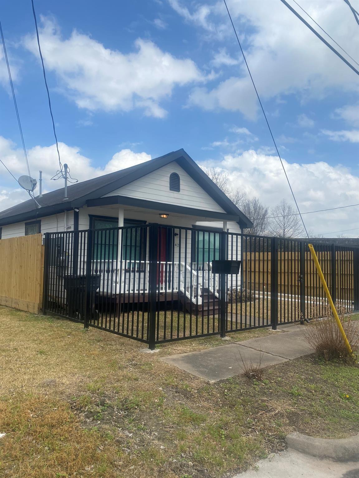 White-sided single-story house with a covered porch enclosed by a black metal fence.