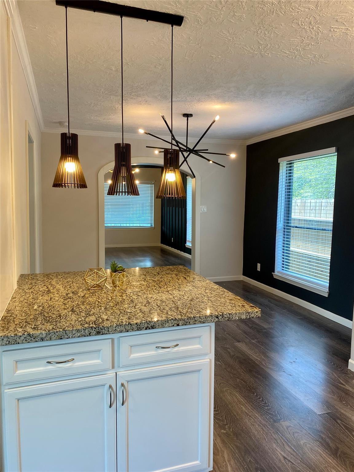 Kitchen island with granite countertop and pendant lights beside a black accent wall and large window.