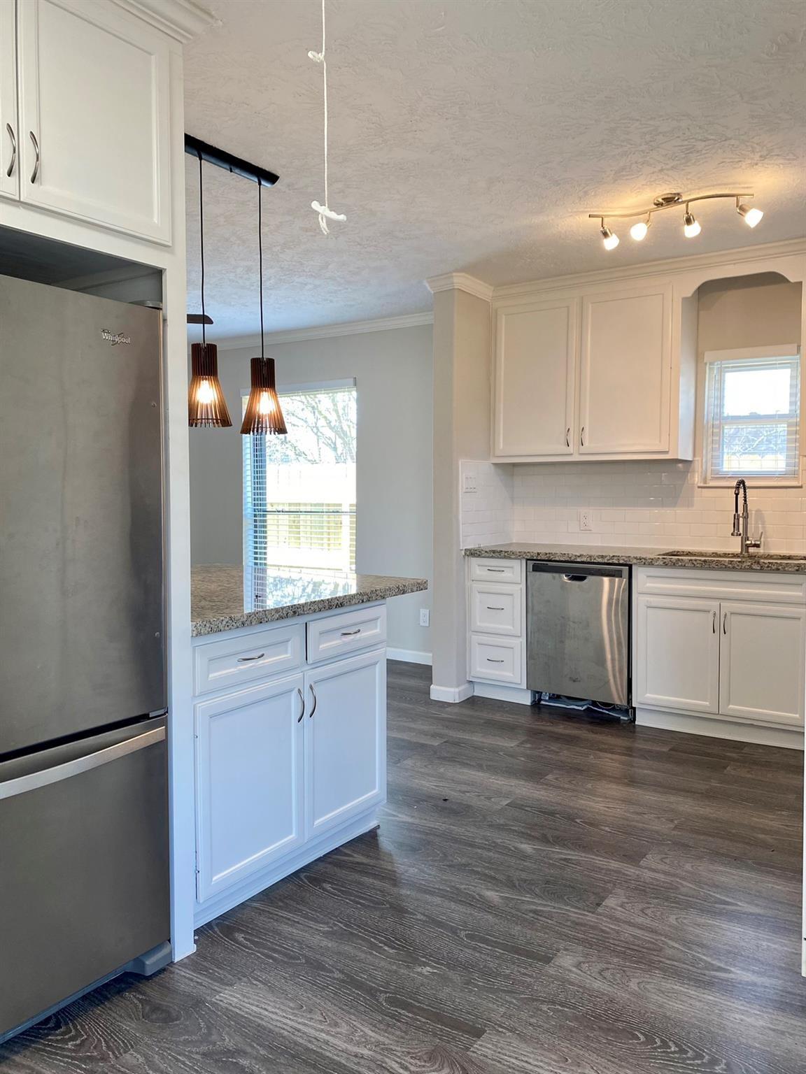 Kitchen with white cabinetry, granite counters, stainless steel appliances, and gray wood-look floors.