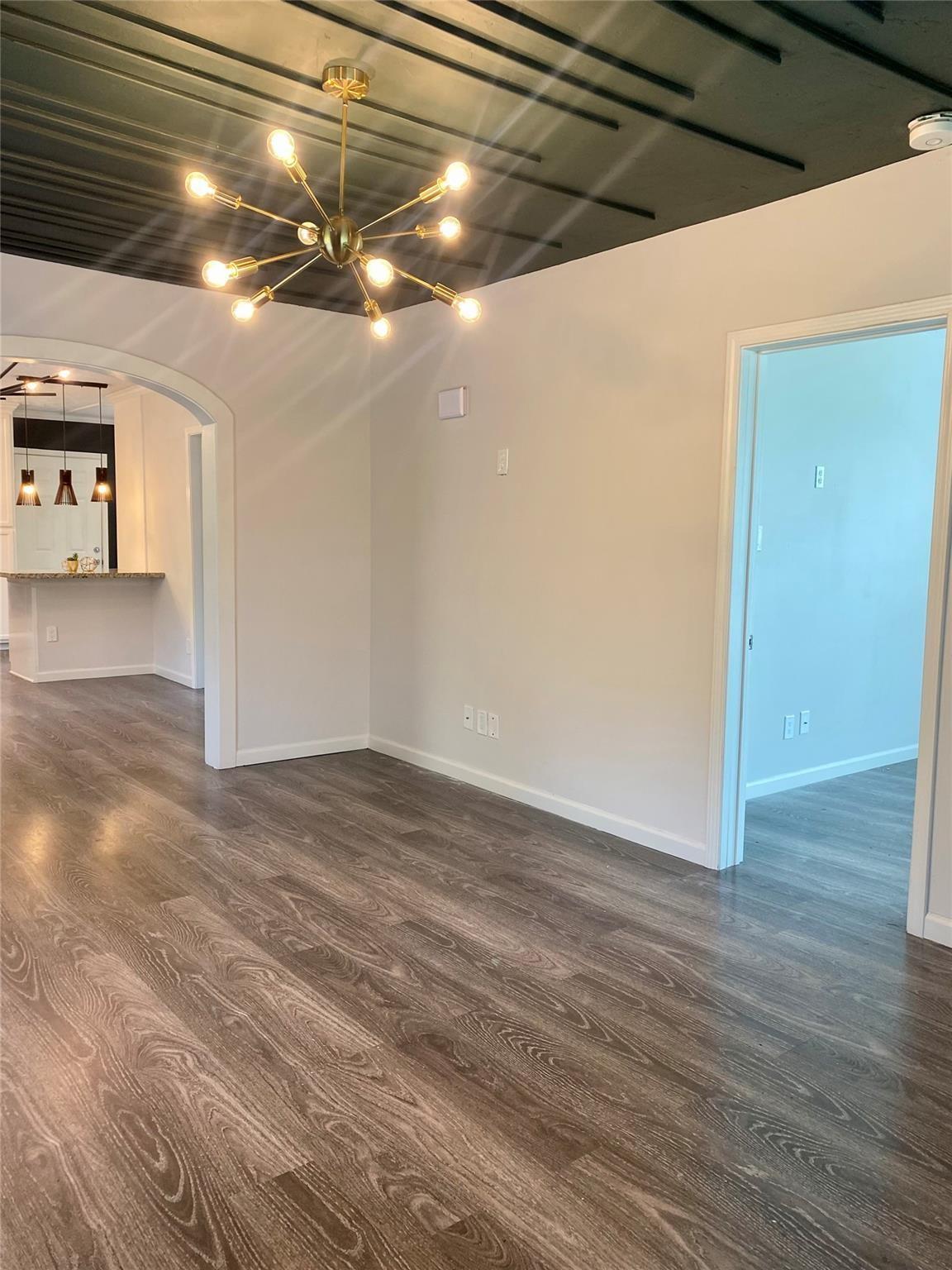 Vacant room with wood-look floors, a dark beamed ceiling, and a brass starburst chandelier.