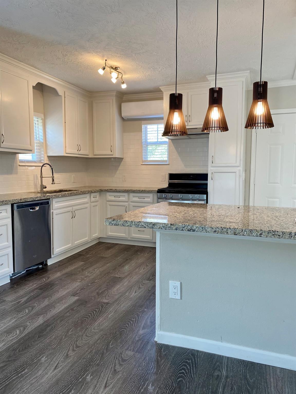 Kitchen with white cabinets, granite counters, a large peninsula, and three pendant lights.