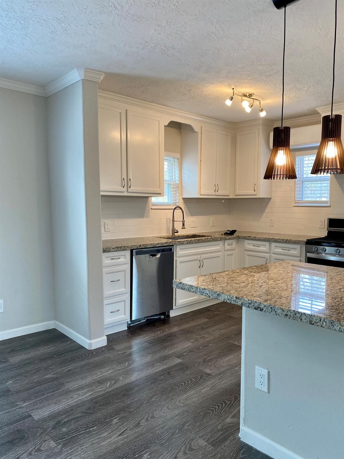 Kitchen with white cabinets, granite island, stainless steel appliances, and dark wood-look flooring.