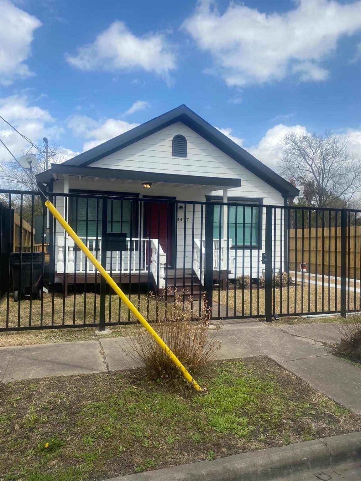 White gable-front house with dark trim and a red door behind a black metal fence.