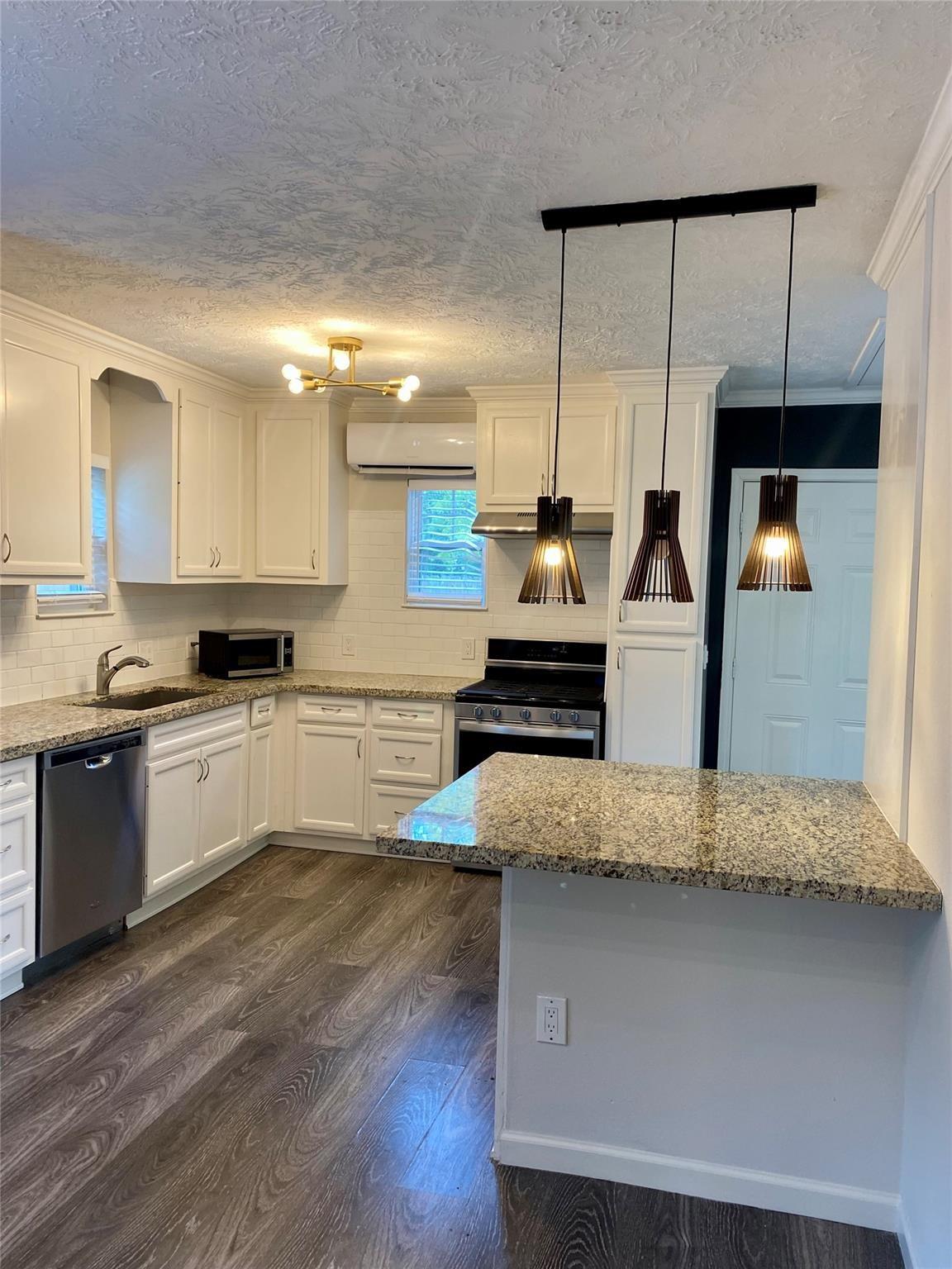 Kitchen with white cabinetry, granite island, stainless steel appliances, and three pendant lights.