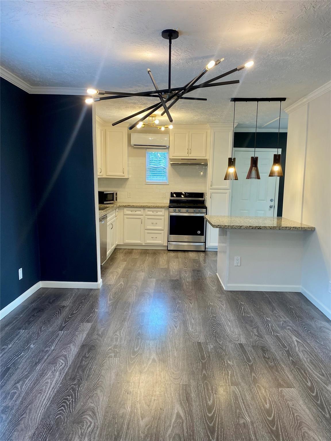 Kitchen with white cabinets, stainless steel appliances, granite counters, and pendant lights beside an empty dining area.