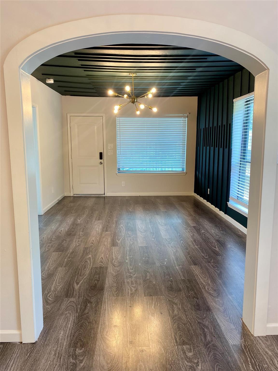 Empty room with an arched entry, dark slatted accent wall and ceiling, and branching chandelier.