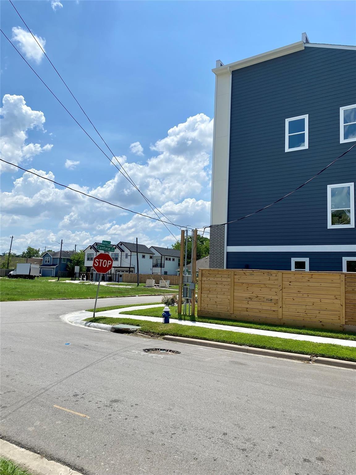 Dark blue multi-story house with white trim and a wooden fence beside a street intersection.