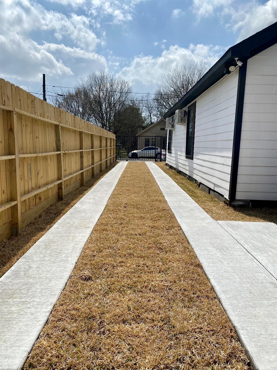 Side yard with parallel concrete paths between a white house and wooden privacy fence.