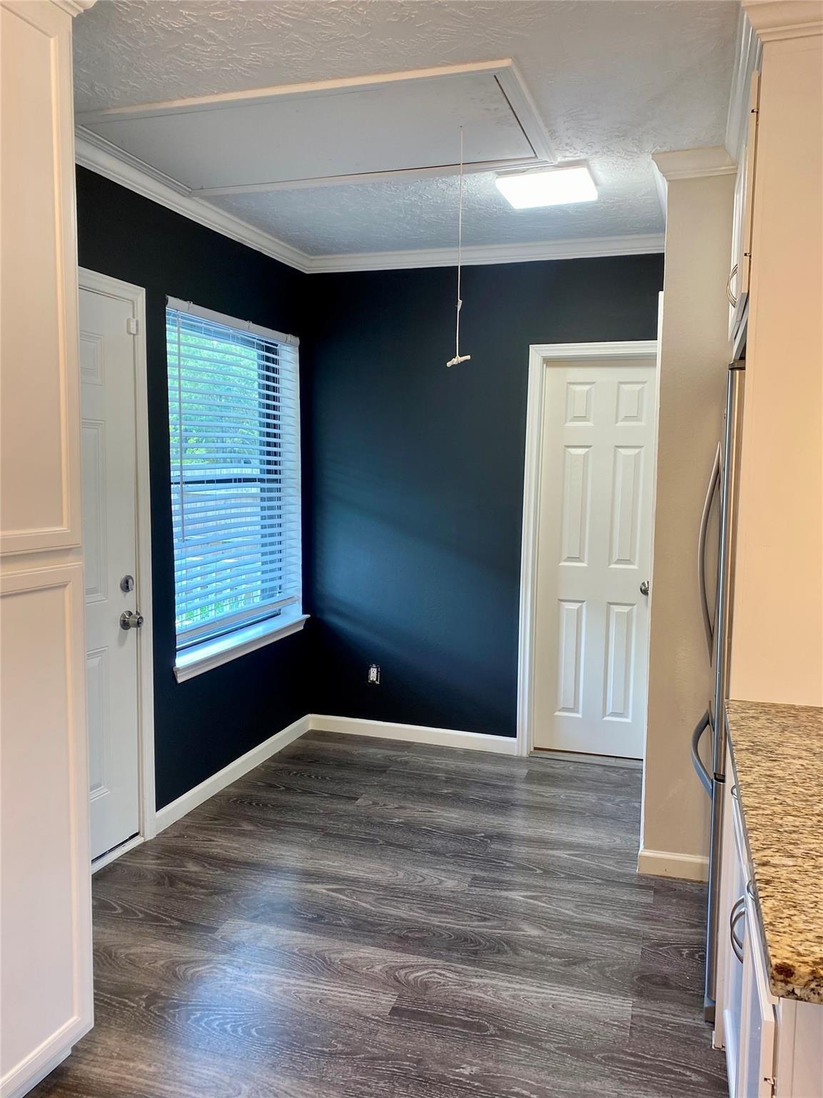 Kitchen nook with dark navy walls, gray flooring, and a window with blinds beside white cabinetry.
