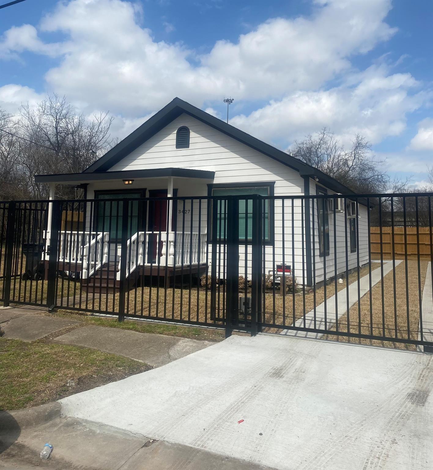 White single-story house with dark trim and a covered porch behind a black metal fence.