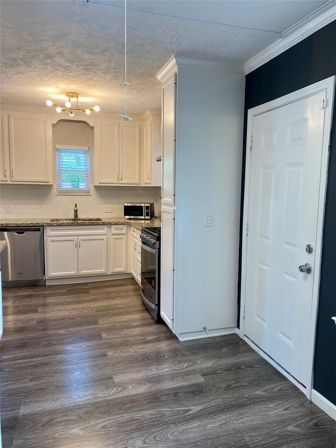Kitchen with white cabinets, stainless steel appliances, and a white door against a dark accent wall.