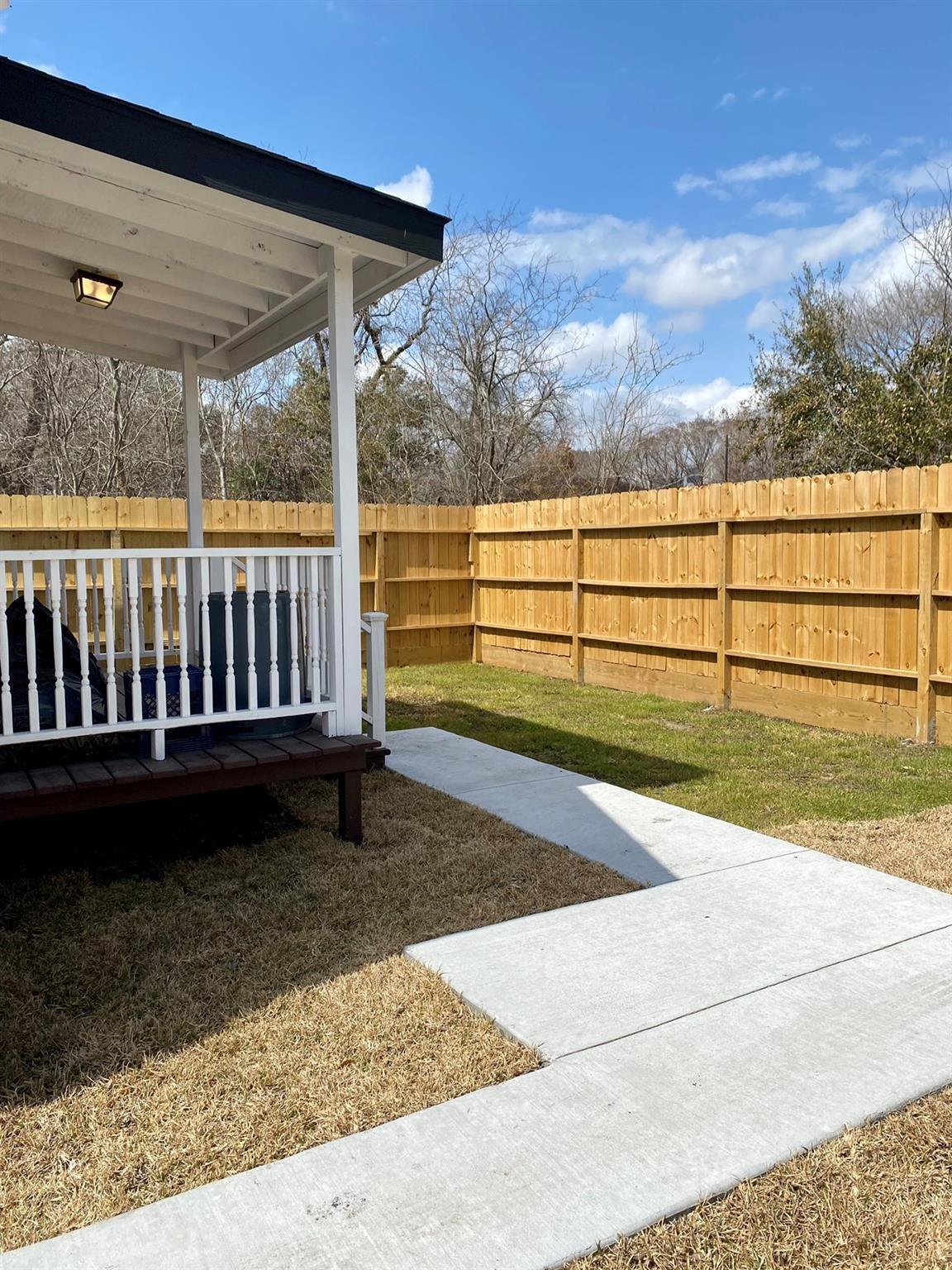 Fenced backyard with a covered porch and concrete walkway through dry grass.